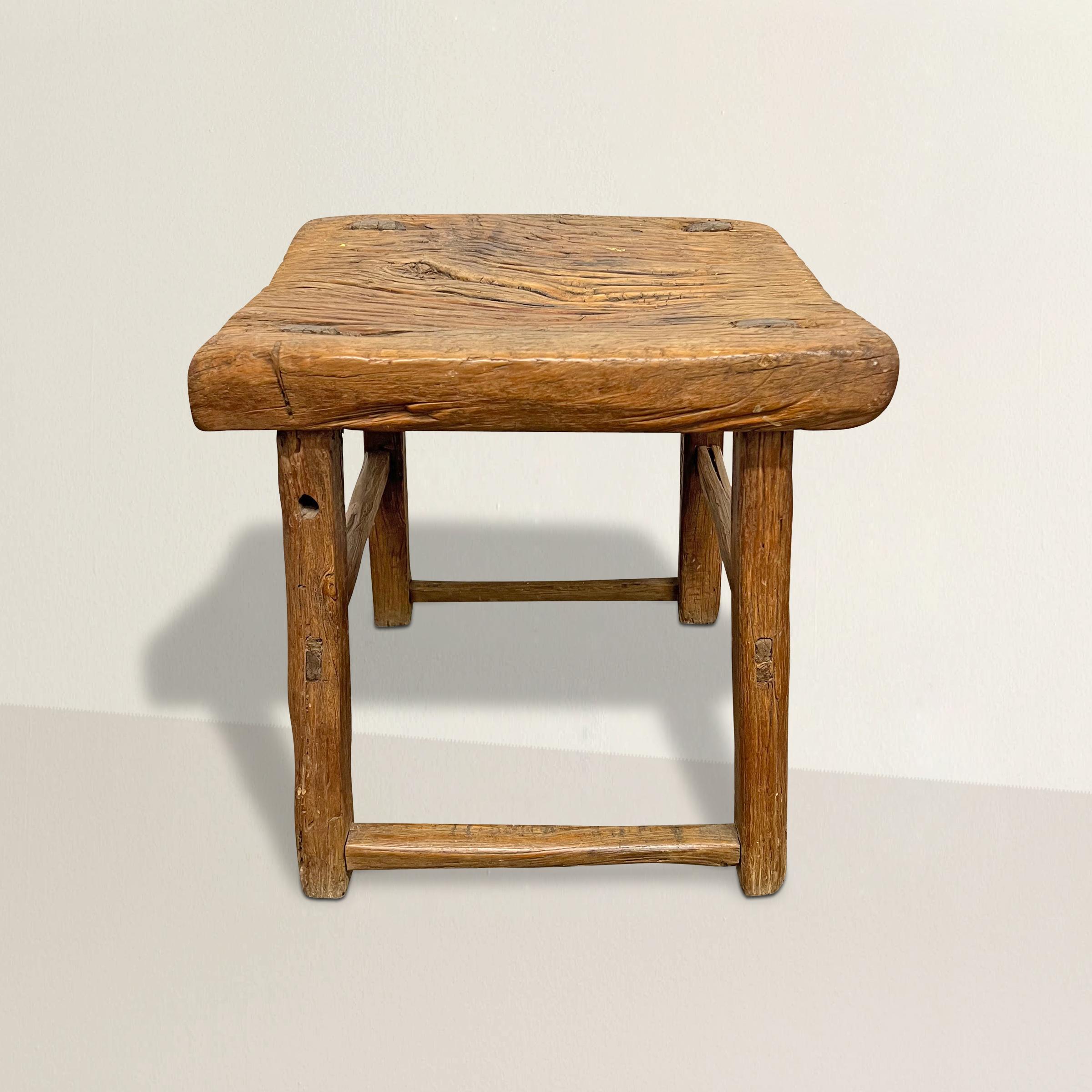 This early 20th-century provincial Chinese stool or side table, expertly crafted from well-weathered elmwood, tells a story etched in its grain and adorned with a patina that only the hands of time could impart. Its versatile design makes it ideal