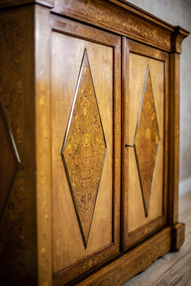 We present you a double-leaf walnut piece of furniture with Avant-corps corners.
The case, same as the doors, is inlaid with floral motifs.
The door panels are smooth, decorated with appliqués in the shape of elongated diamonds, which are inlaid,