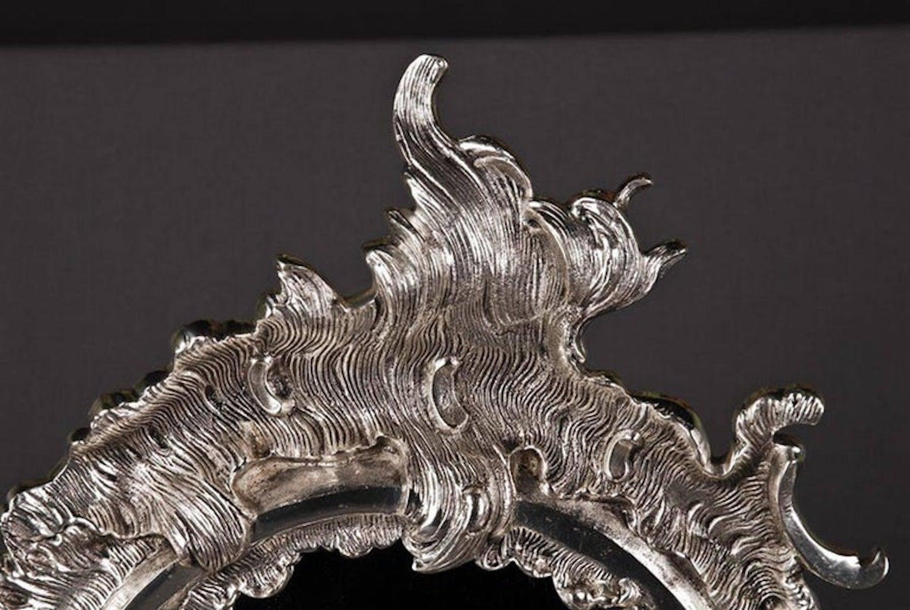 Delicato specchio da parete in stile rococò.
Bronzo, finemente inciso e dorato in argento. Cornice dello specchio a forma di Rocaille. 