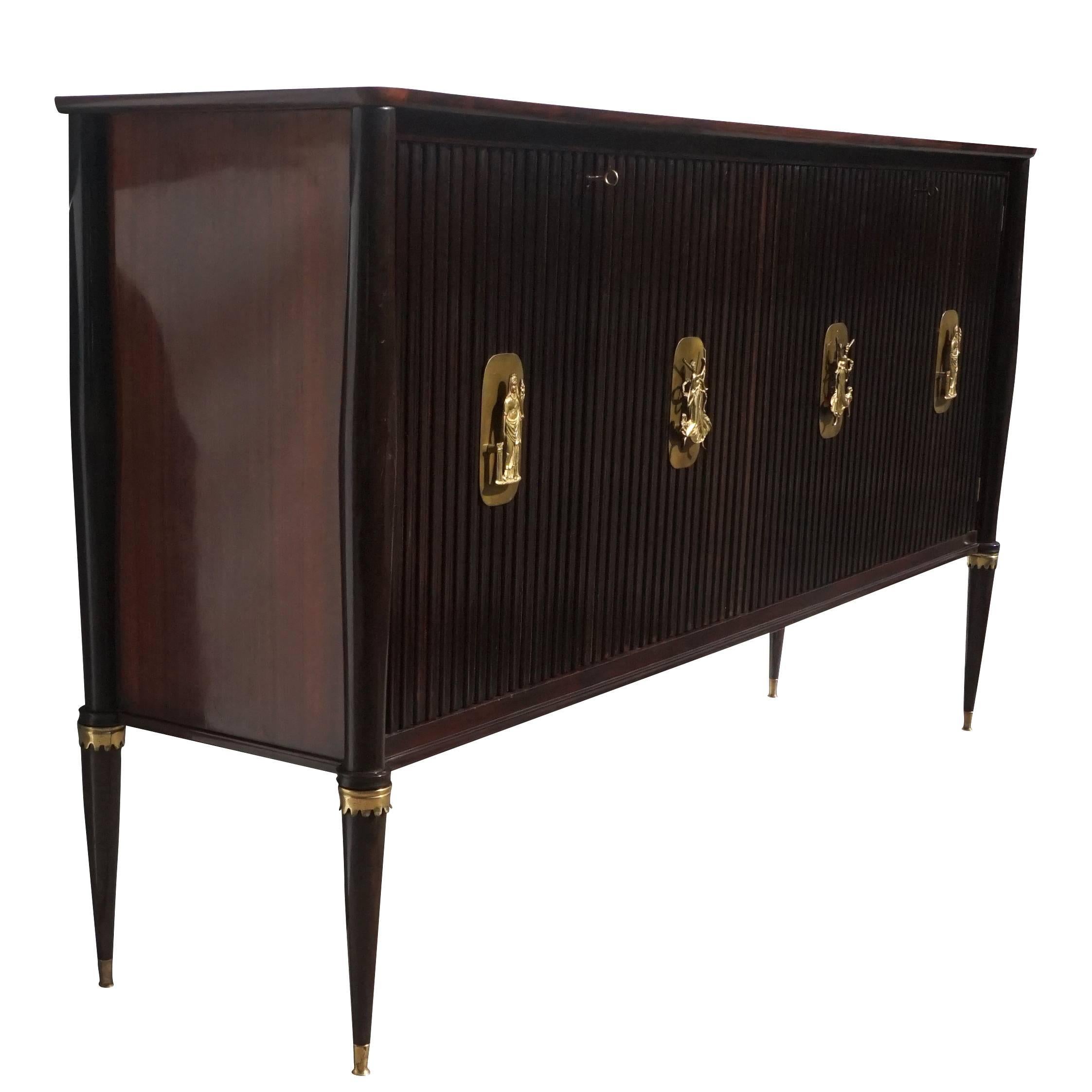 A very spectacular bar cabinet made of hand carved rosewood with sliding doors opening to a world of nightstands and different planets. The outside panels are rosewood with massive guilted bronze hardware. Designed by Osvaldo Borsani in good