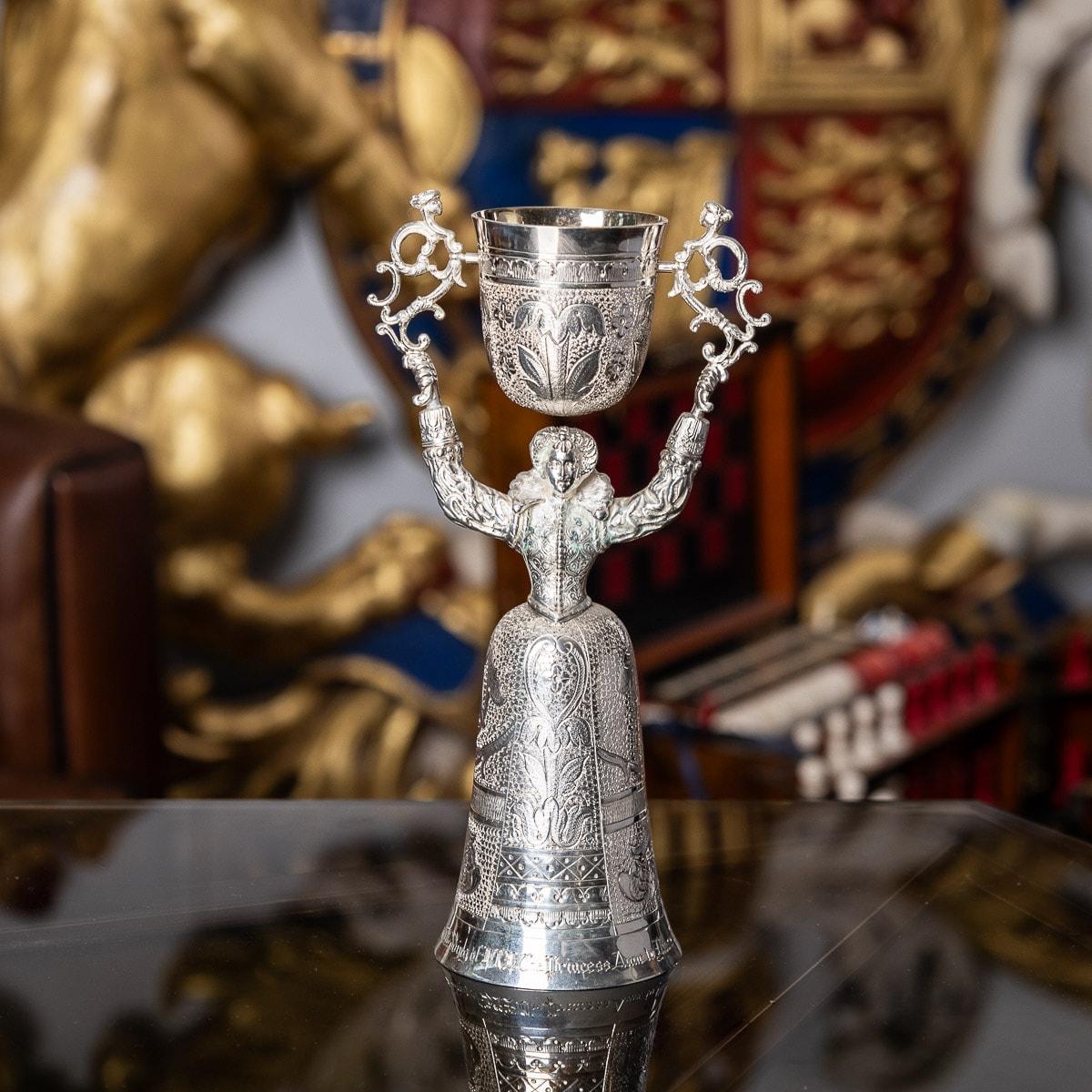 Novelty 20th century solid silver wager / marriage cup, the cups design inspired by the early 16th century German example, modelled as a female figure supporting over her head a smalled domed swiveling cup and the lower cups half chased with