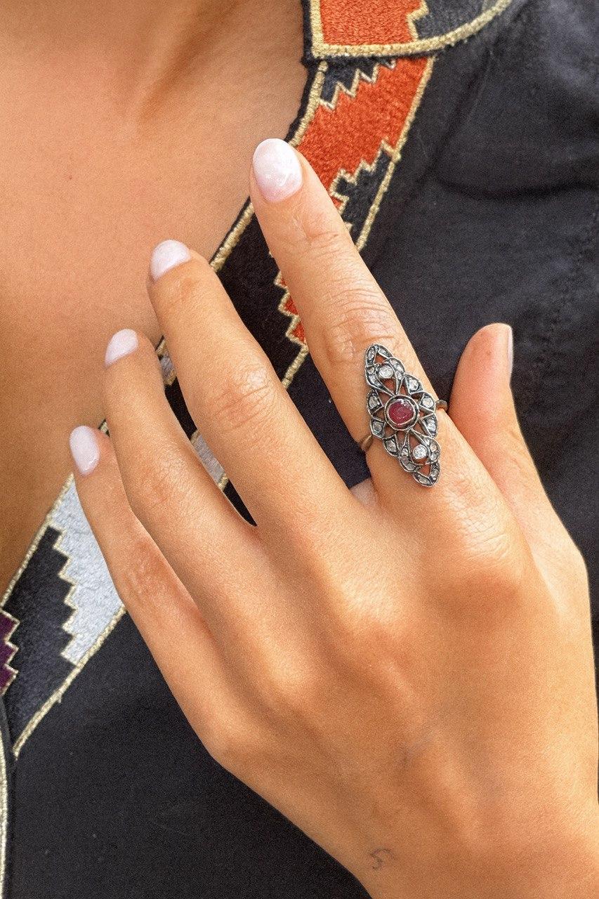 This exquisite vintage ring carries the timeless charm of antique design. At its center lies a natural round ruby, glowing with a vivid red hue — a symbol of love and strength. The ruby is elegantly framed by delicate rose-cut diamonds set in an