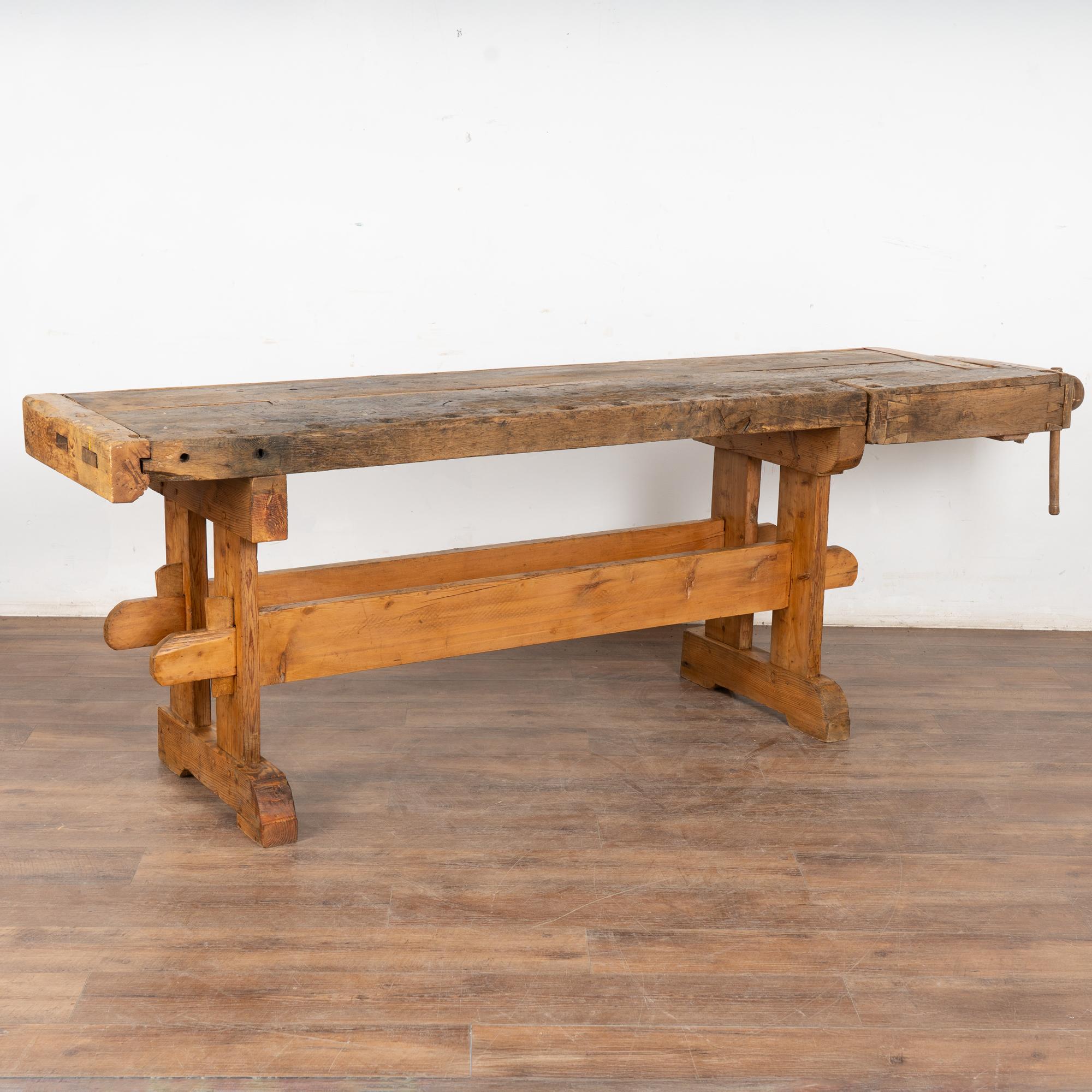 La patina usurata di questo autentico banco da lavoro per falegnami riflette la sua età e gli anni di utilizzo. Ogni ammaccatura, graffio, sgorbia, perdita di vernice e macchia arricchisce il carattere e il fascino di questo vecchio tavolo da