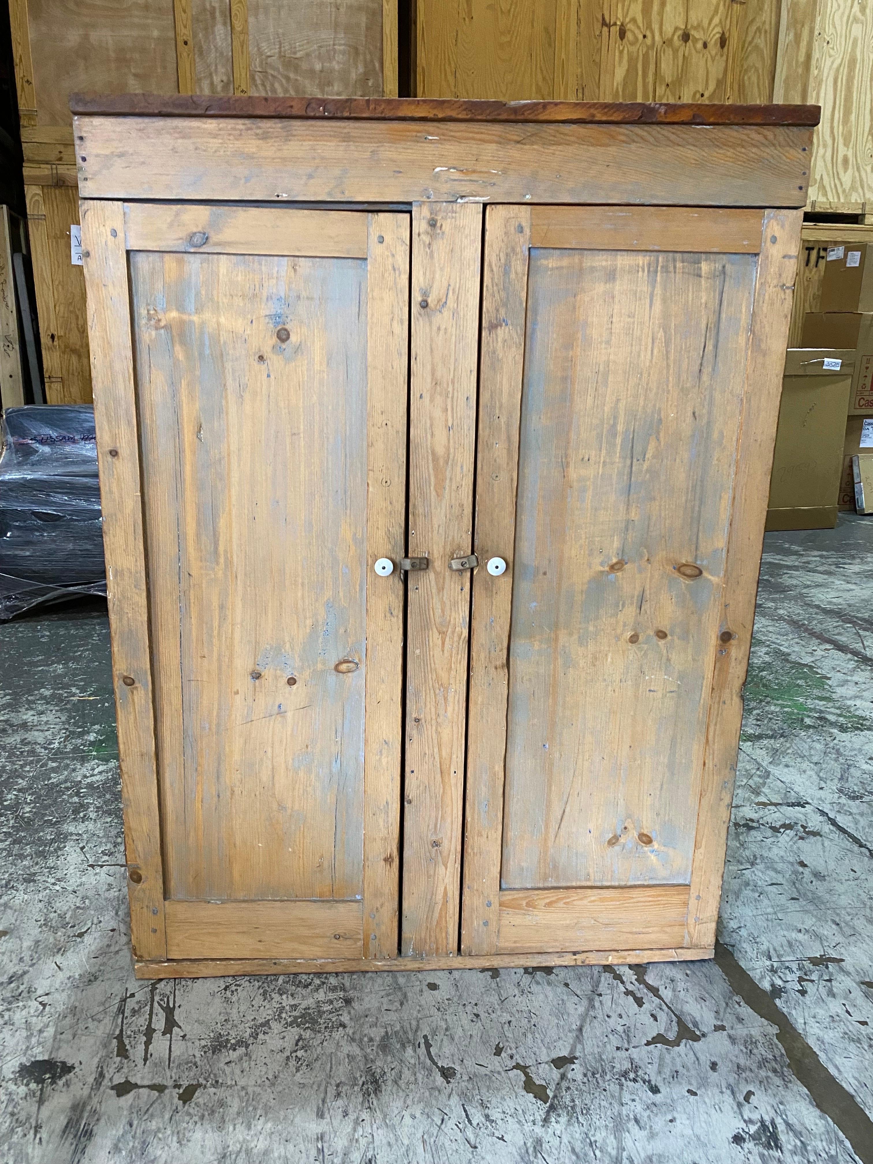 Armoire en pin rustique du 20e siècle 
Une armoire en pin de construction simple avec deux portes et un rail central. Un lavage peint grisâtre donne une belle patine. Deux boutons en porcelaine et des loquets en bois. Cinq étagères composées de deux