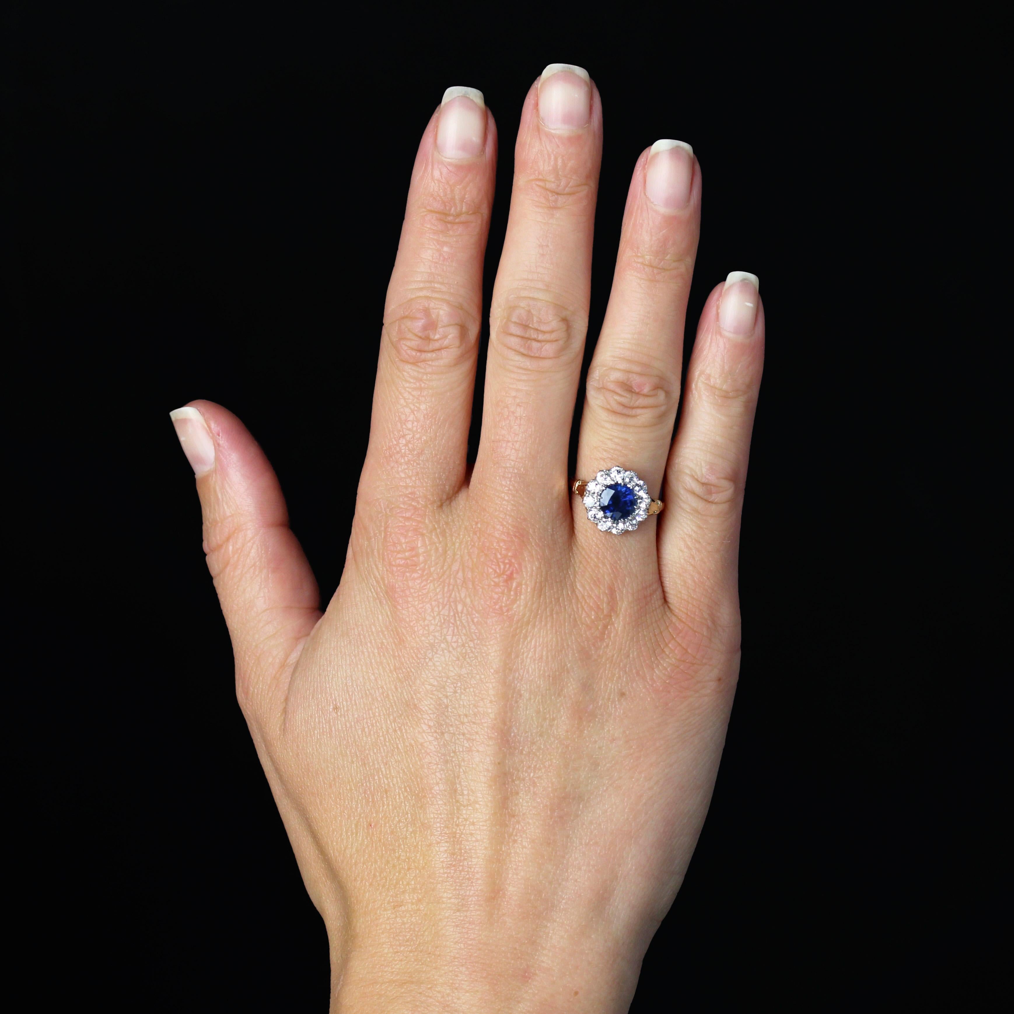 Anello in oro giallo 18 carati e platino.
Un anello a fiore senza tempo, la cui montatura rotonda è incastonata al centro da uno zaffiro blu intenso trattenuto da griffe, circondato da diamanti antichi taglio brillante anch'essi trattenuti da