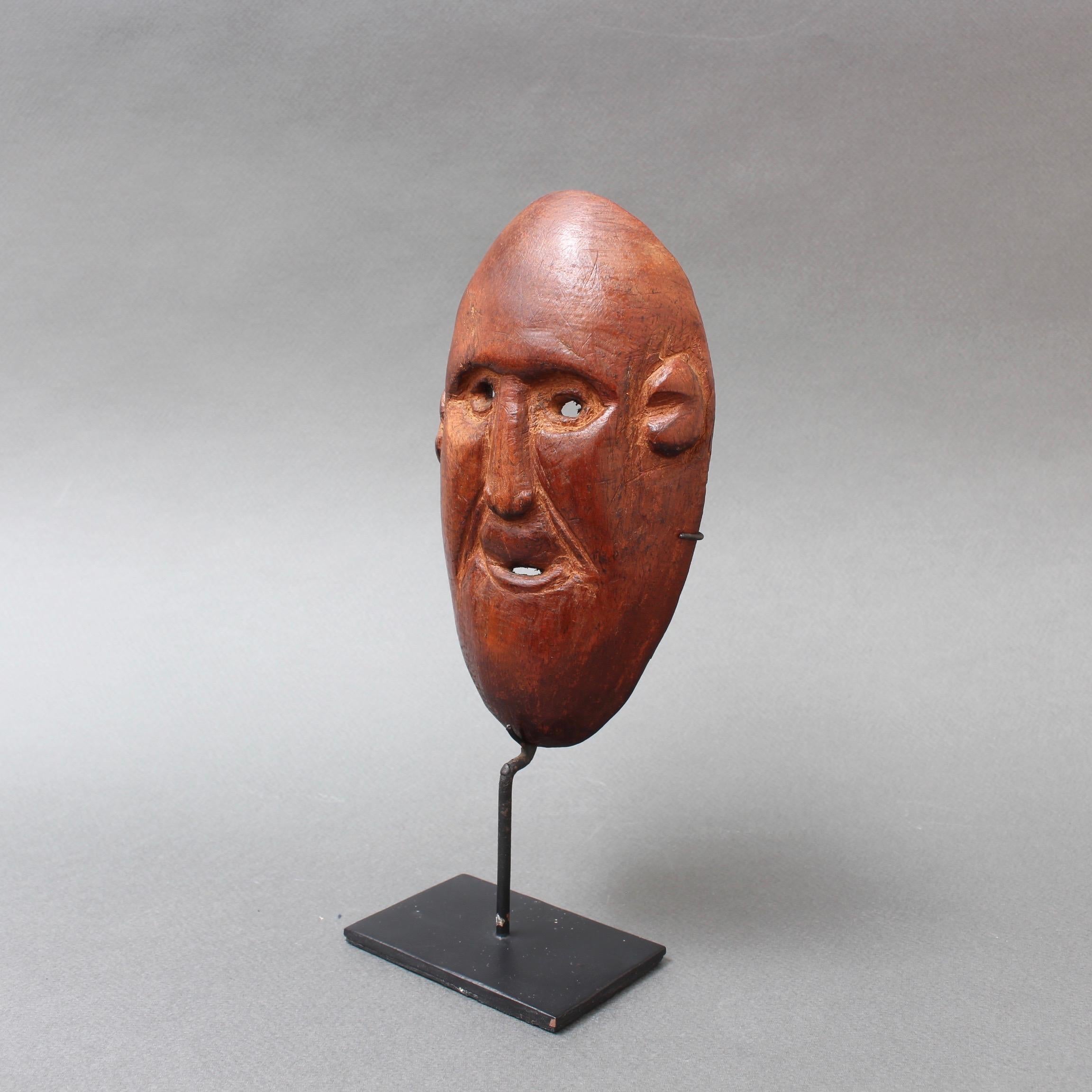Timor Island sculpted wooden traditional mask (circa 1960s-1970s) on contemporary stand. This is a traditional mask of a figure with male facial features and two holes as eyes and another for the mouth. The island of Timor gave rise to a distinctive