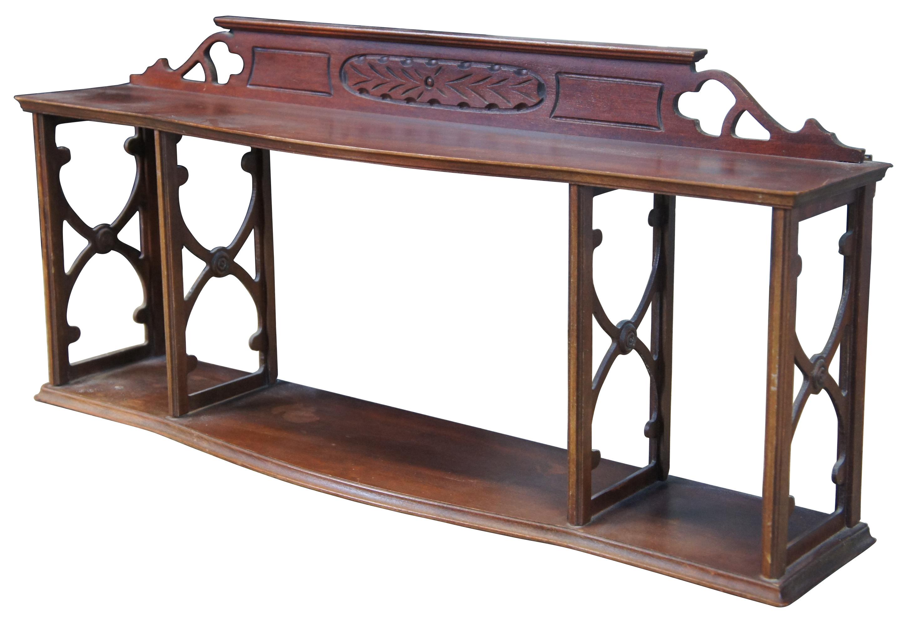 Mid-20th century serpentine wall hanging shelf. Made from mahogany with an open frame featuring x shaped fretwork and pierced backsplash. Includes button shaped medallions and a carved backsplash. 

Measures: 29.75