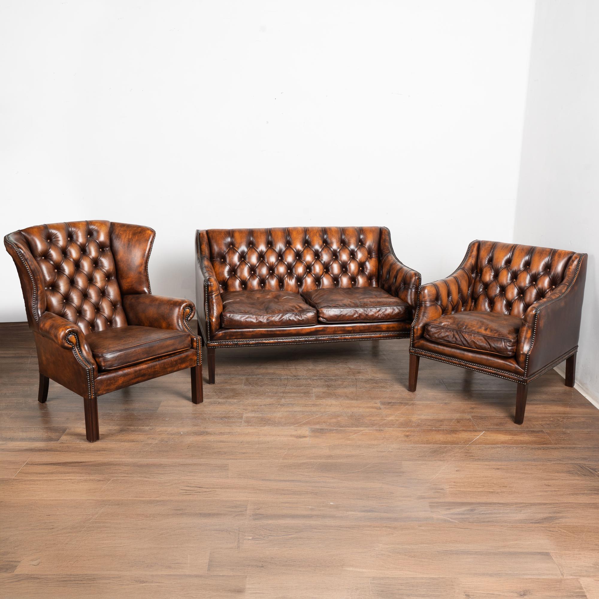 Set of (3) vintage leather Chesterfield style two seat sofa, wingback armchair and club armchair.
The mottled brown leather shows darker and lighter shades blending together; leather is in good condition and accented by brass nail heads and