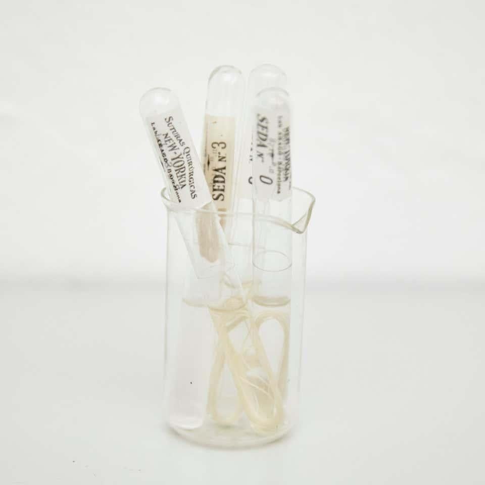 Jeu de coutures chirurgicales vintage du 20e siècle  Par un fabricant inconnu, Espagne.    En état d'origine, avec une usure mineure conforme à l'âge et à l'utilisation, préservant une belle patine.    Matériaux :  Verre  Suture en soie   