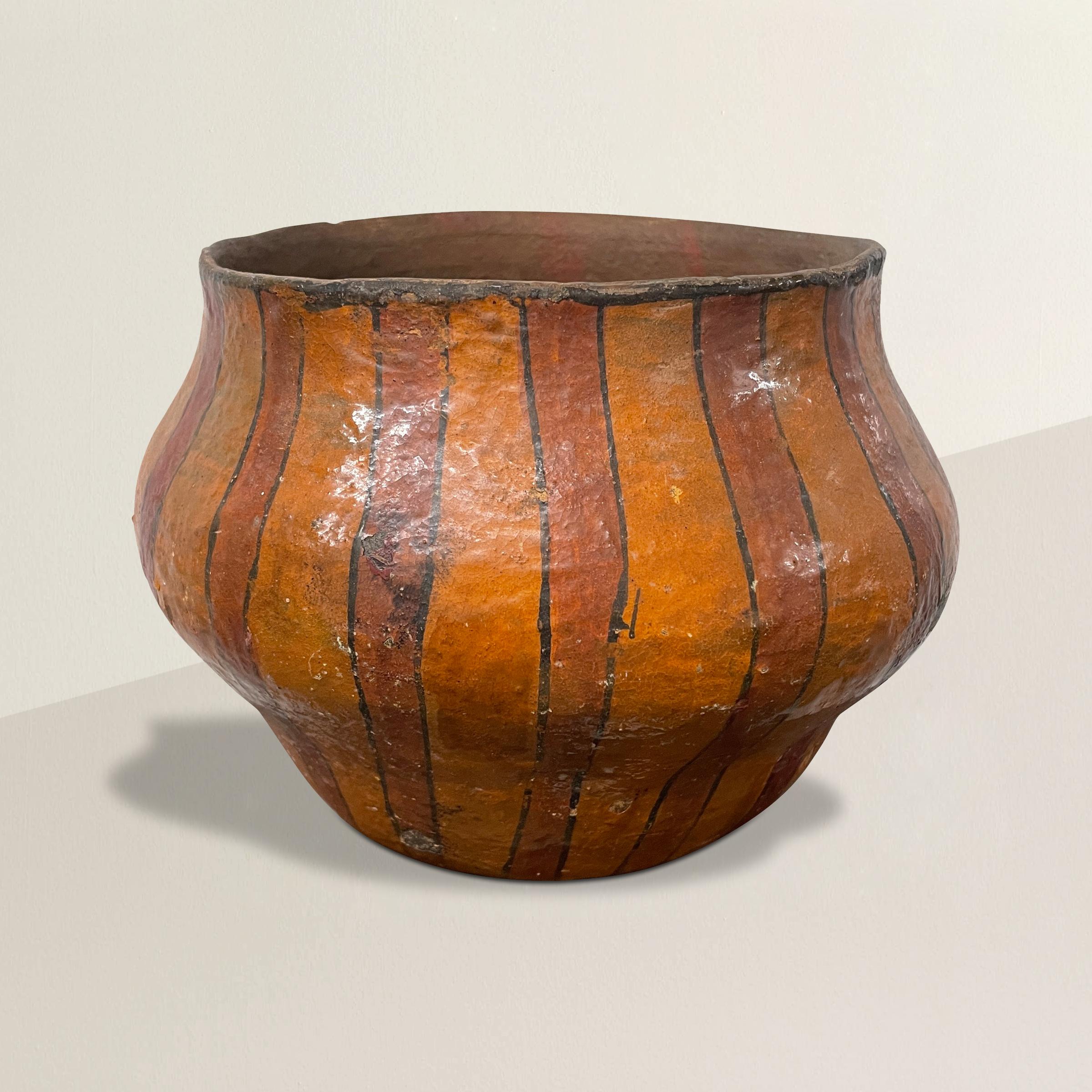 Un saisissant pot Shipibo amazonien du 20e siècle, fabriqué à la main en argile, décoré de larges lignes rouges et oranges, et vernissé du saphir d'un arbre. Les membres de la tribu Shipibo créent le pot, généralement décoré de motifs géométriques