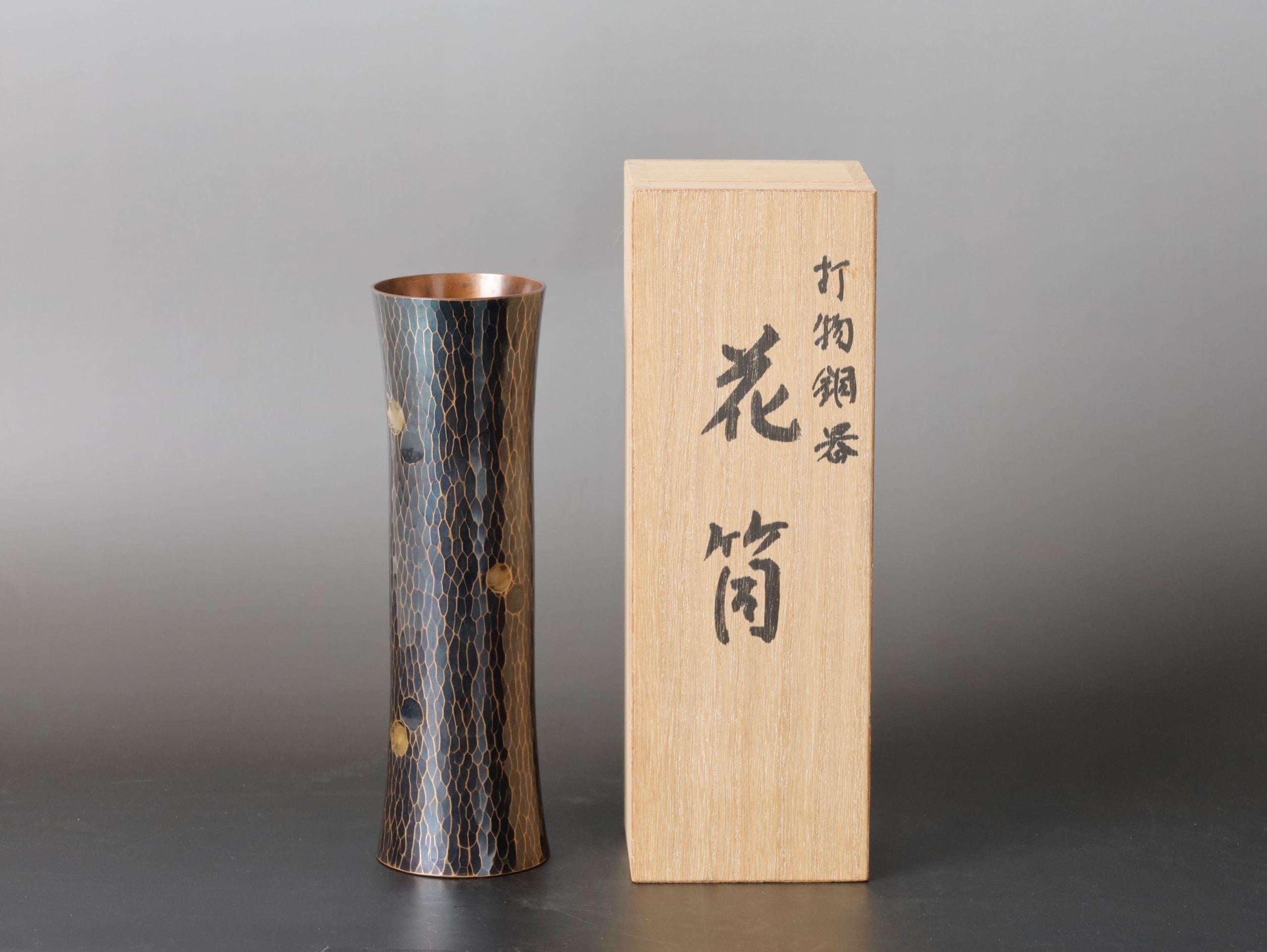 Ce vase en cuivre exquis est une pièce unique du Japon, martelée à la main au XXe siècle par Kyuhoudou. Le vase a une hauteur de 18 cm (7 pouces), un diamètre de 5,5 cm (2,1 pouces) et pèse 360 g (0,8 lbs). Il est livré avec sa boîte en bois