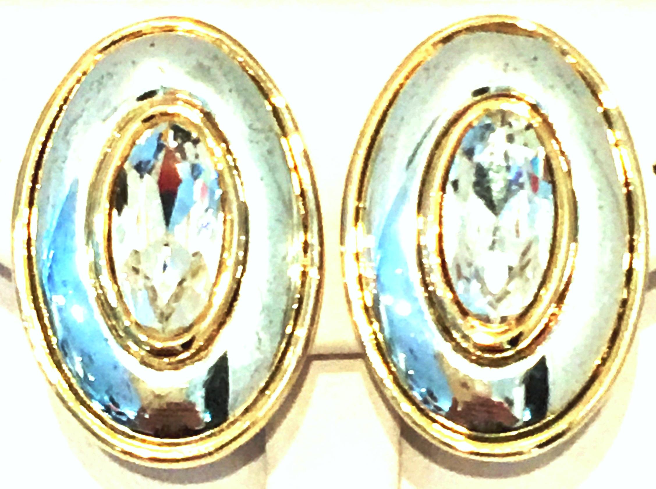 20th Century Modernist Two Tone Gold & Silver Plate Swarovski Crystal Earrings By, Givenchy. These clip style dimensional earrings features a gold plate ground with silver plate accent and cabochon set oval Swarovski crystal colorless central stone.