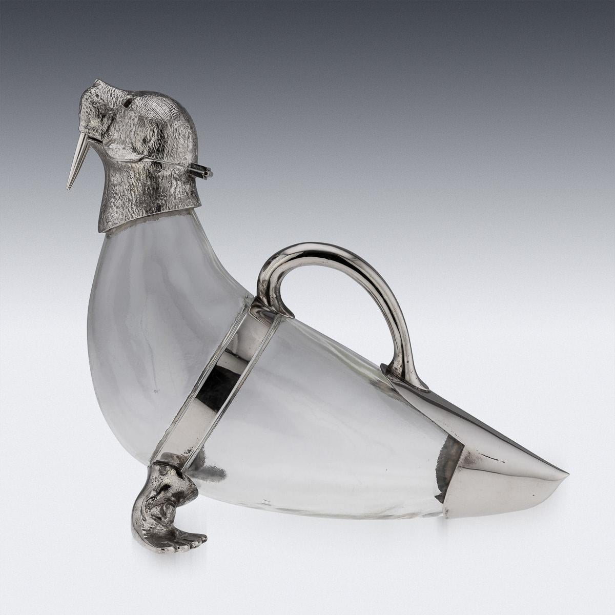 Mid 20th Century zoomorphic silver-plated and glass walrus wine jug is a true marvel of artistry and craftsmanship. This stunning piece seamlessly blends the elegance of silver with the delicacy of glass, resulting in a wine jug that is both