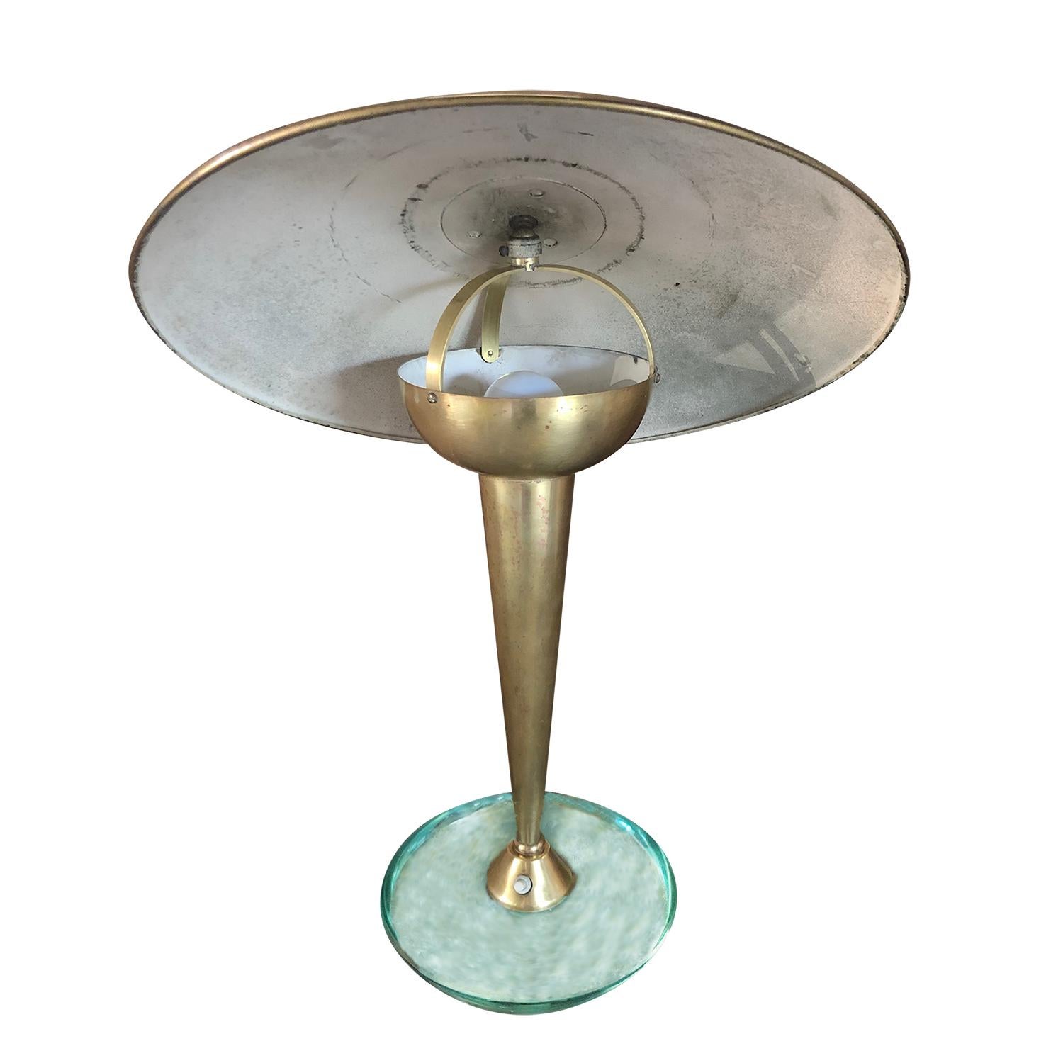 A small, vintage Mid-Century Modern Italian table lamp or desk lamp made of hand crafted brass, standing on a thick, circular light green Murano glass base. Produced by Stilnovo in good condition. The light shade is adjustable, featuring a one light