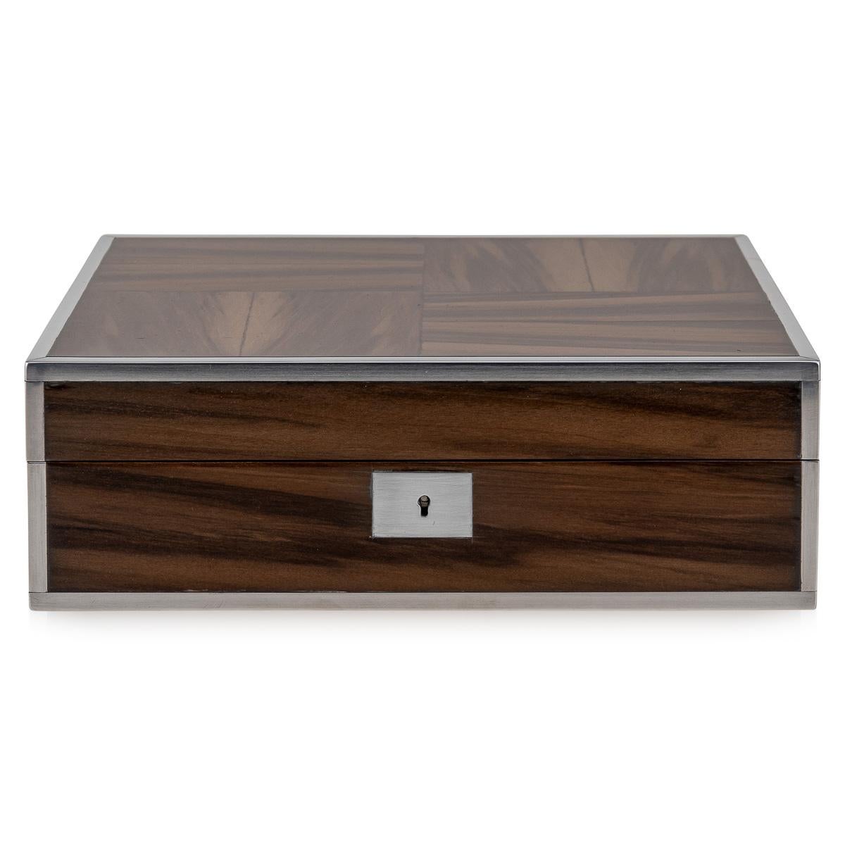 Featuring a sleek contemporary design, this piece showcases smoked walnut veneer over a solid walnut structure, complemented by sturdy stainless steel hinges and a lock adorned with aluminium accents. Upon opening, it reveals a meticulously crafted