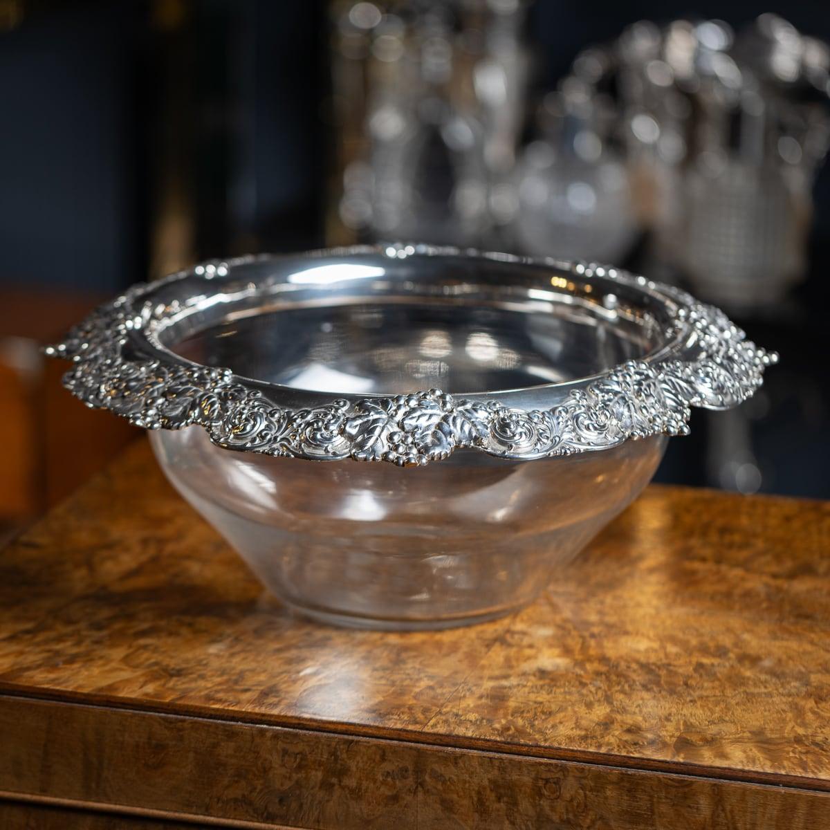 A 20th Century American solid silver & glass bowl made by the world renowned Tiffany & Co. The glass is plain and of a tapering circular shape. The rim is applied with a silver collar, featuring embossed entwining grapes and vines. Made by Tiffany &