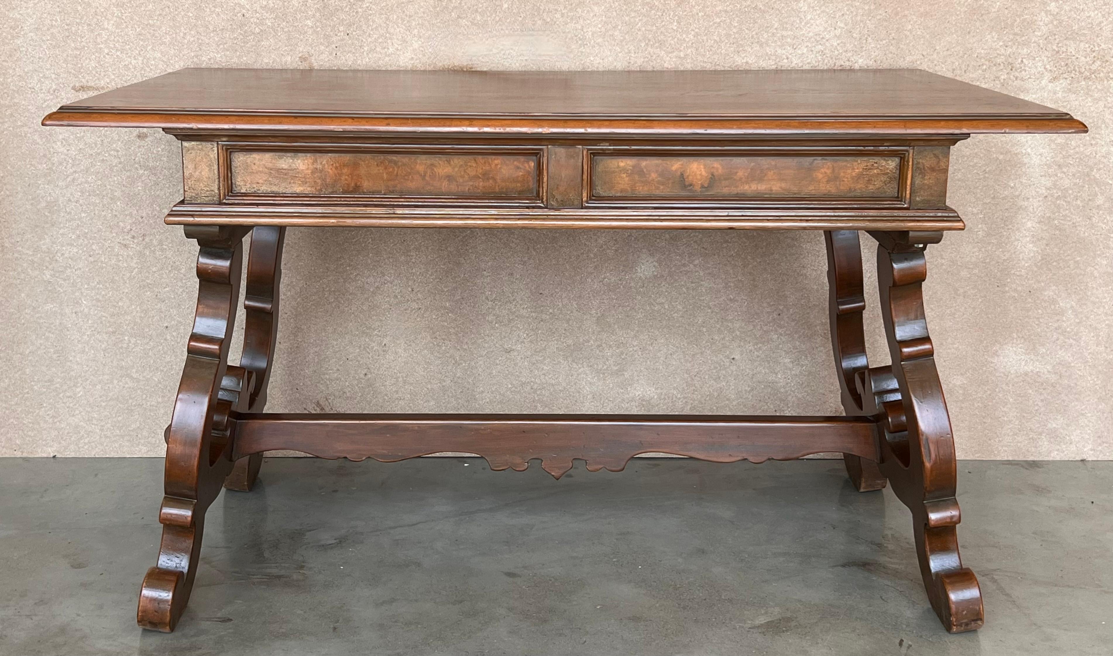 An 20th century Spanish baroque desk, or writing table made of solid walnut with lyre shaped legs joined by wood stretchers. Hand carved decoration across the front and the back. Two drawers with original iron drawer pulls. The top is made from a