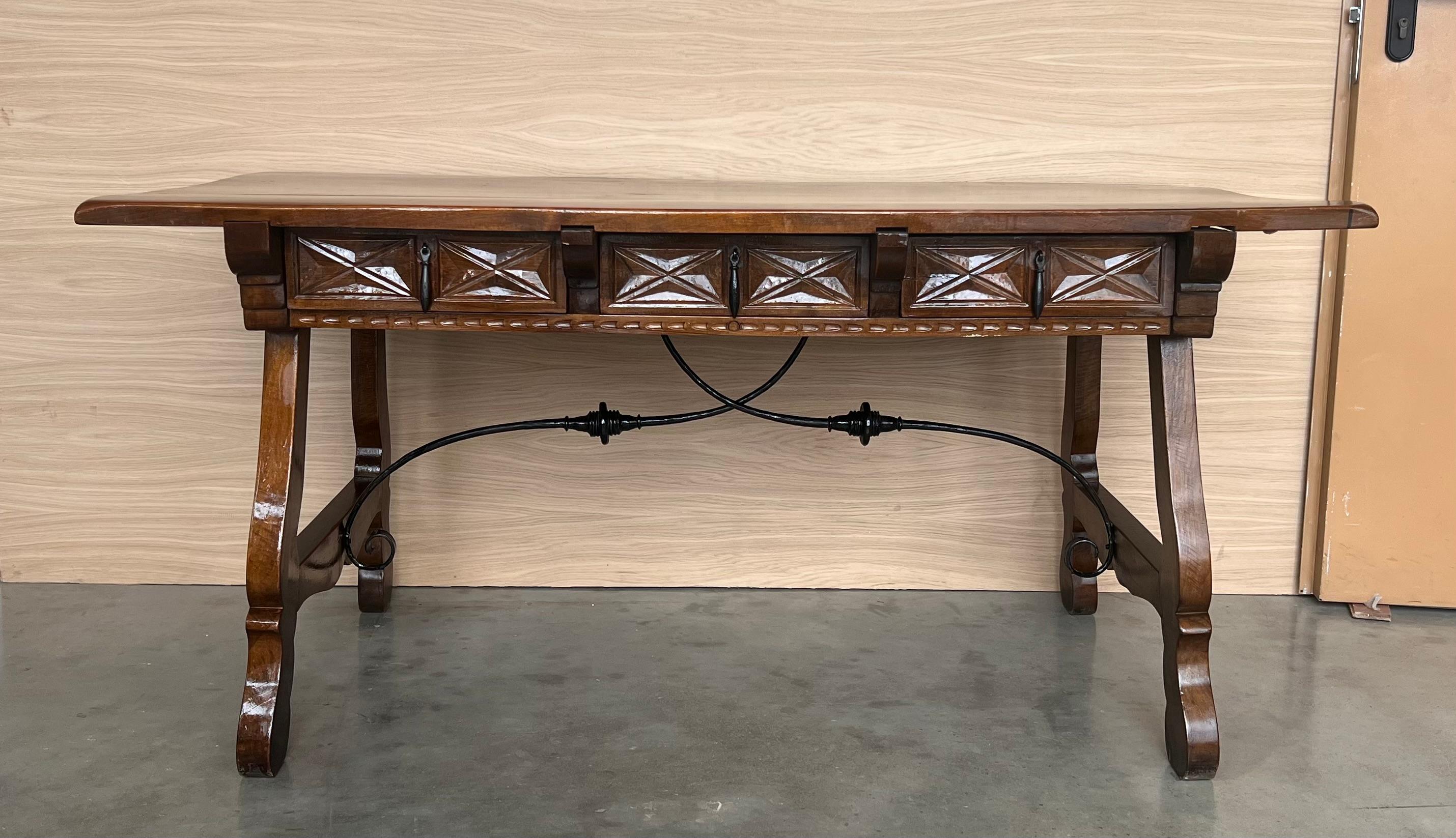 20th Century Spanish baroque desk, or writing table made of solid walnut with lyre legs joined by wrought iron stretchers. Three drawers with original iron drawer pulls. The top is made from a single plank of walnut and is slightly warped. Beautiful