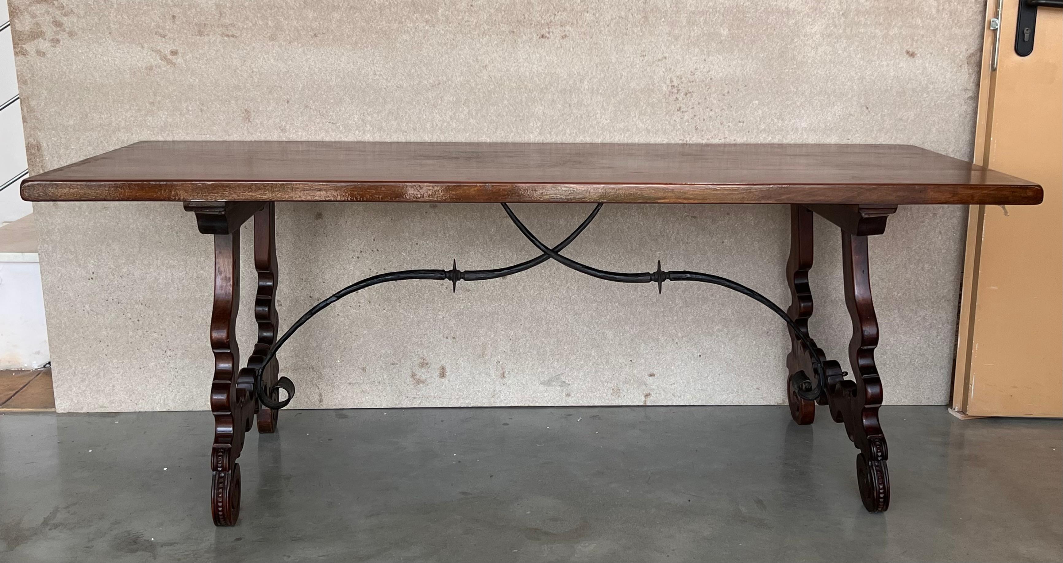A monumental 20th century Spanish trestle table, having a rectangular framed solid walnut inset board top, resting on hand carved, classical lyre legs joined by four beautifully iron stretchers.
The legs have a handmade carved with typical motifs