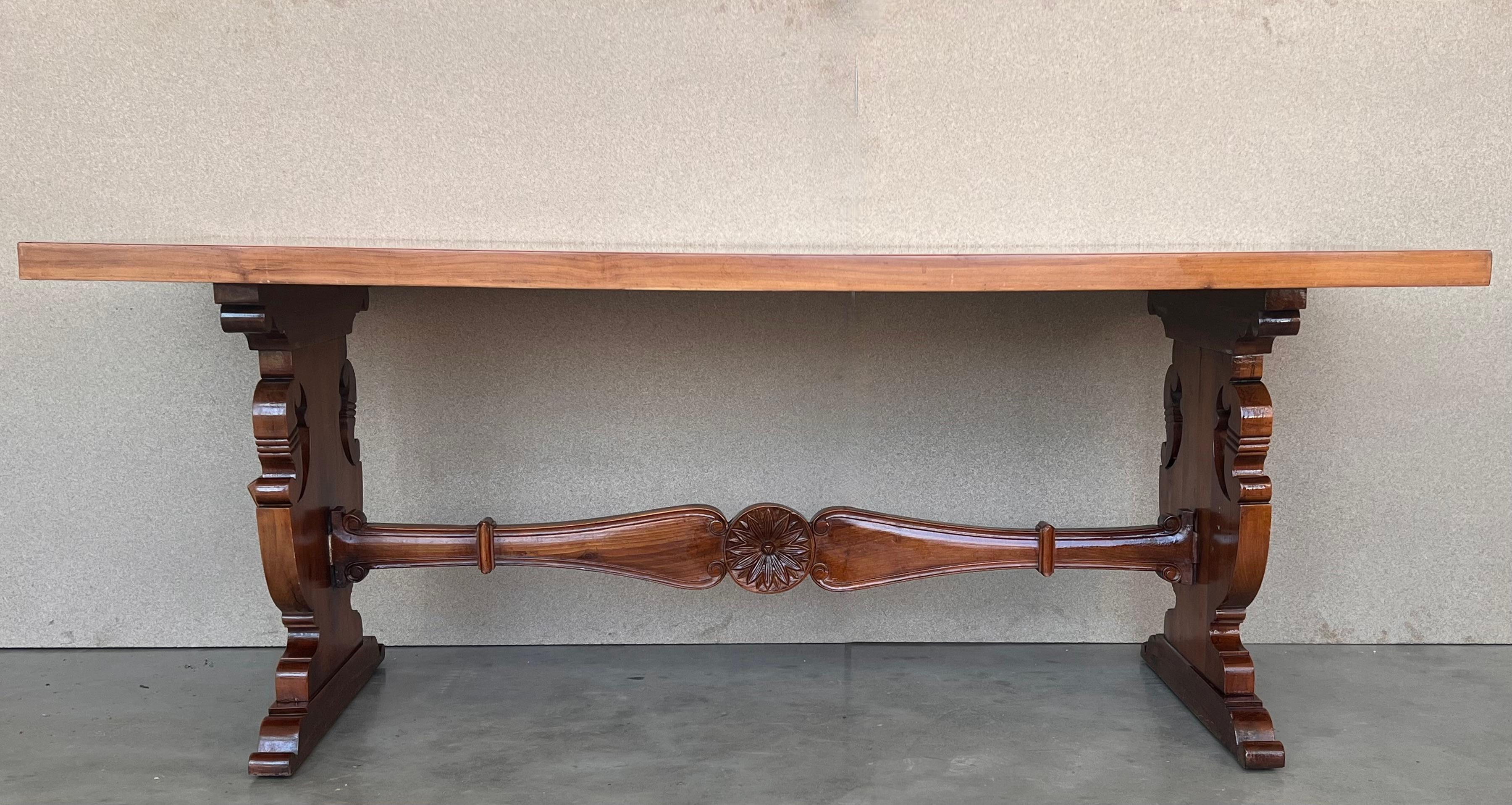 Une table à tréteaux espagnole monumentale du 20e siècle, avec un plateau rectangulaire encadré en noyer massif, reposant sur des pieds lyre classiques sculptés à la main, reliés par une belle civière en bois.

 