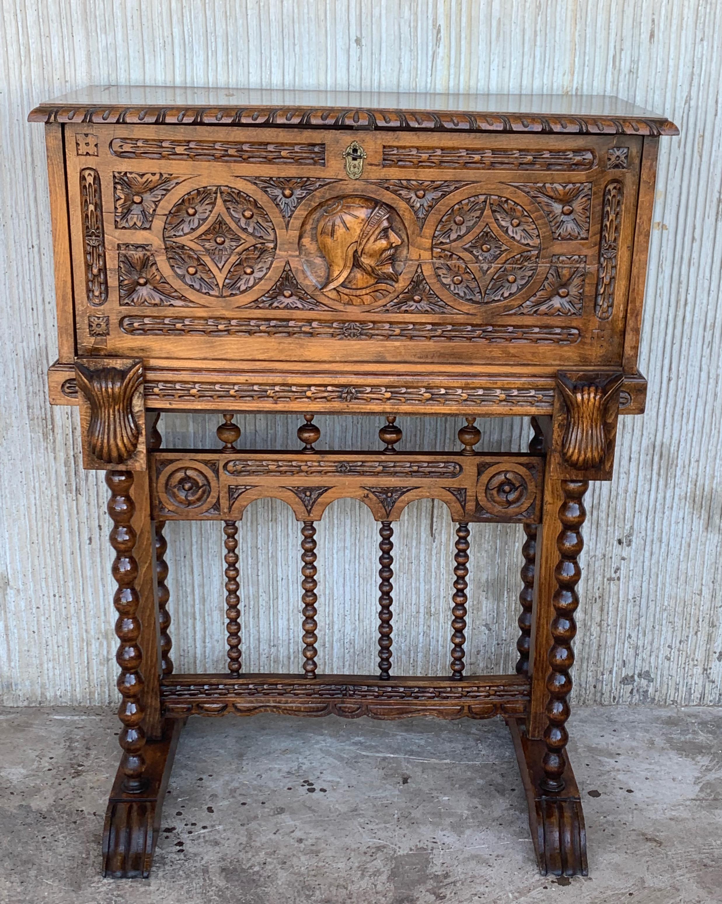 This Bargueno is embellished with a carving head of Don Quixote de la Mancha bordered with branches of leaves. The desk is supported by a pedestal joined by a bridge of turned columns. The front legs contain a carving of two wind god heads with an