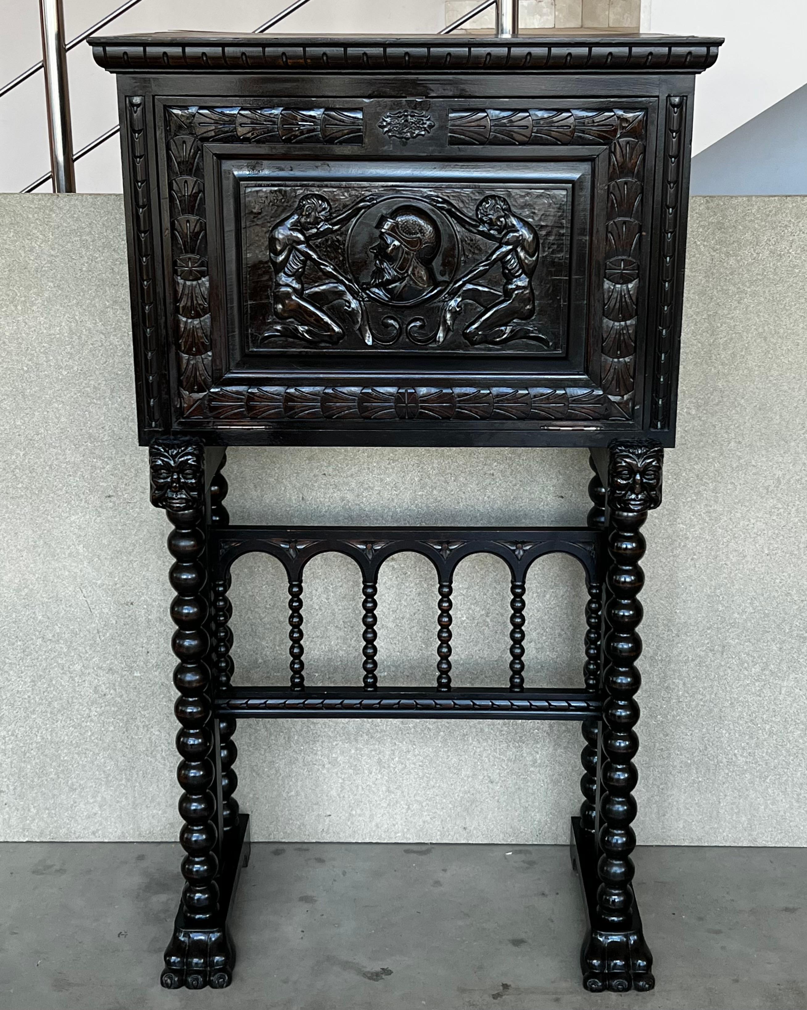 This Bargueno is embellished with a carving of Don Quixote de la Mancha bordered with branches of leaves. The desk is supported by a pedestal joined by a bridge of turned columns. The front legs contain a carving of two wind god heads with an