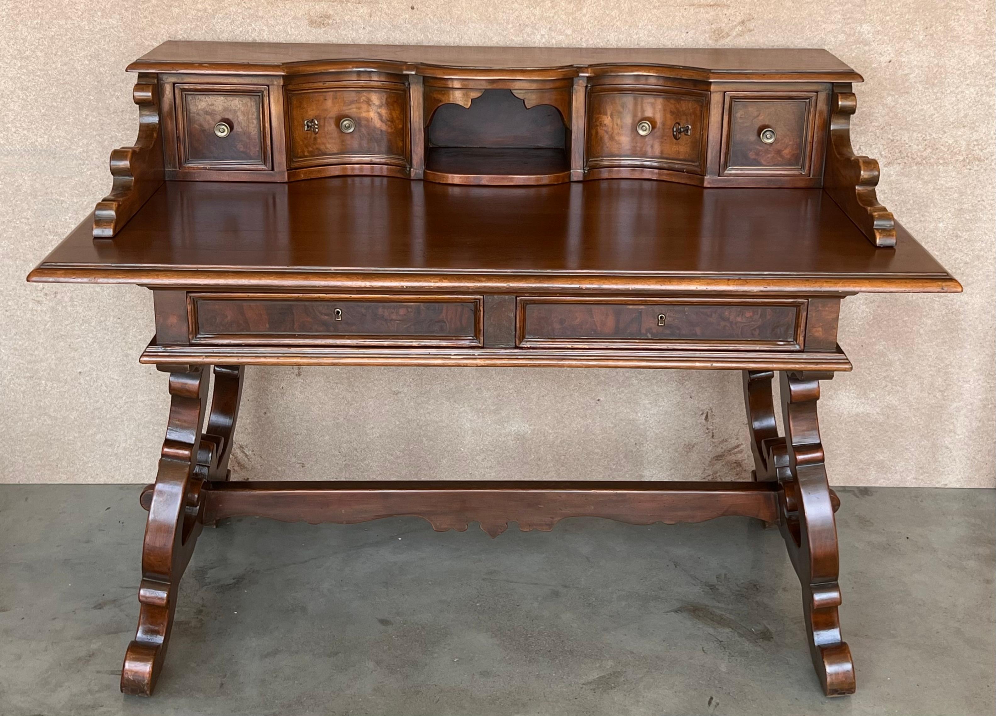 An 20th century Spanish baroque desk, or writing table made of solid walnut with lyre shaped legs joined by wood stretchers. Hand carved decoration across the front and the back. Two drawers with original iron drawer pulls. The top is made from a
