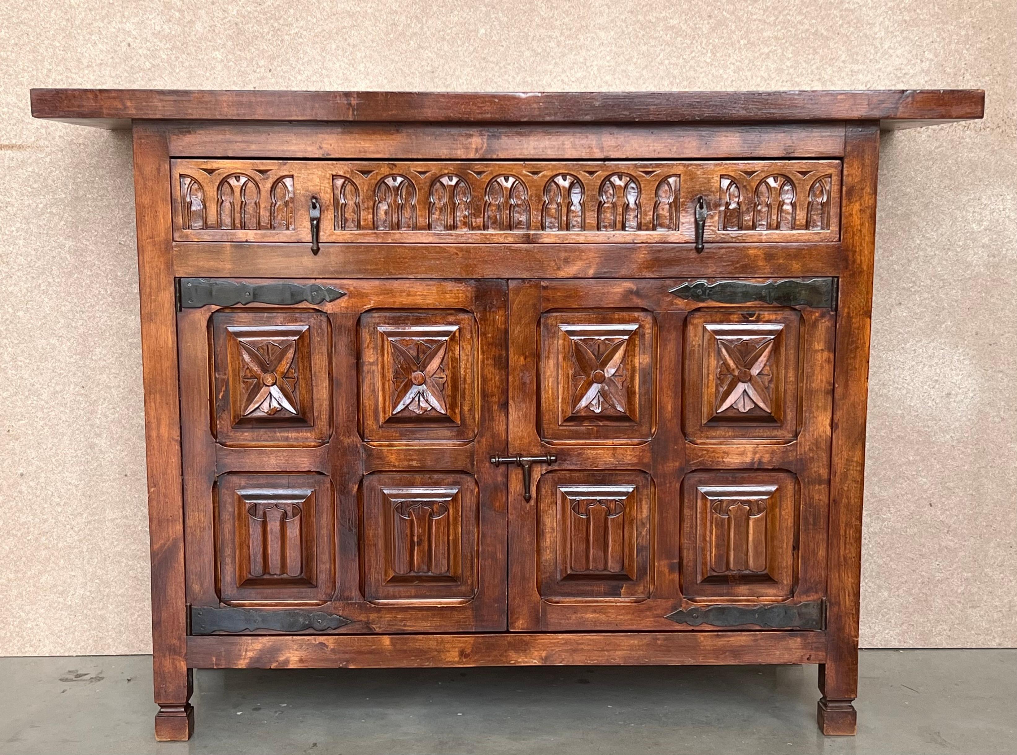 From Northern Spain, constructed of solid walnut, the rectangular top with molded edge atop a conforming case housing one-drawer over two doors, the doors paneled with solid walnut, raised on a plinth base and both parts carved with geometrical