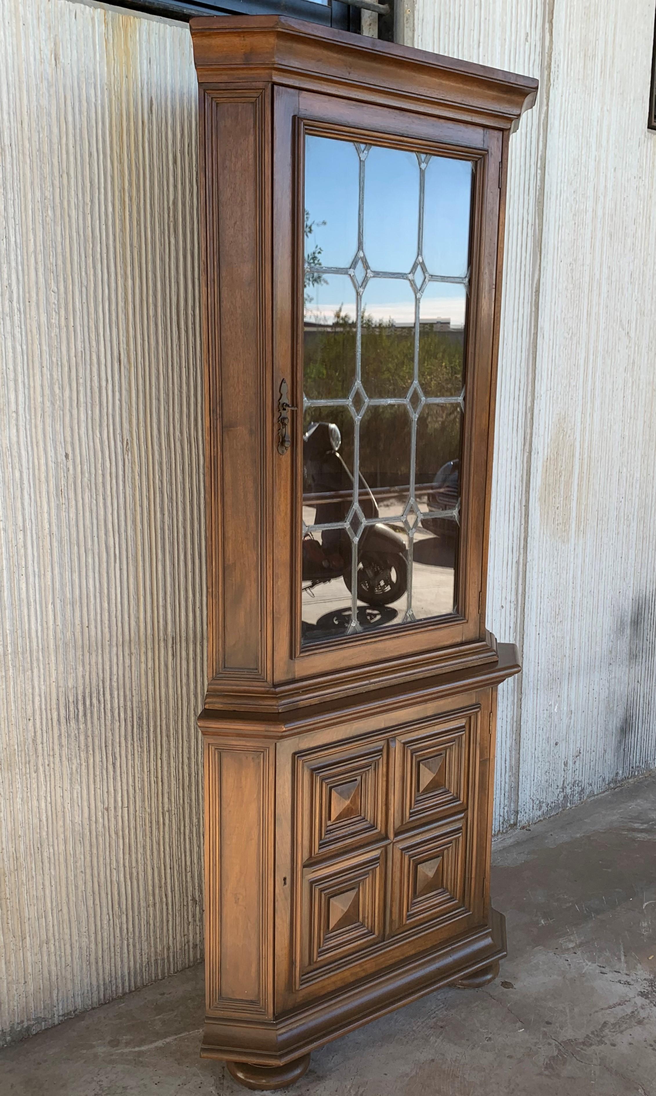 A Spanish Colonial vitrine cabinet from the 20th century in walnut with scalloped base and reeded sides and door. Original lock with key. Original glass. and lead solders. The upper section contains three shelves, the top shaped and slotted for