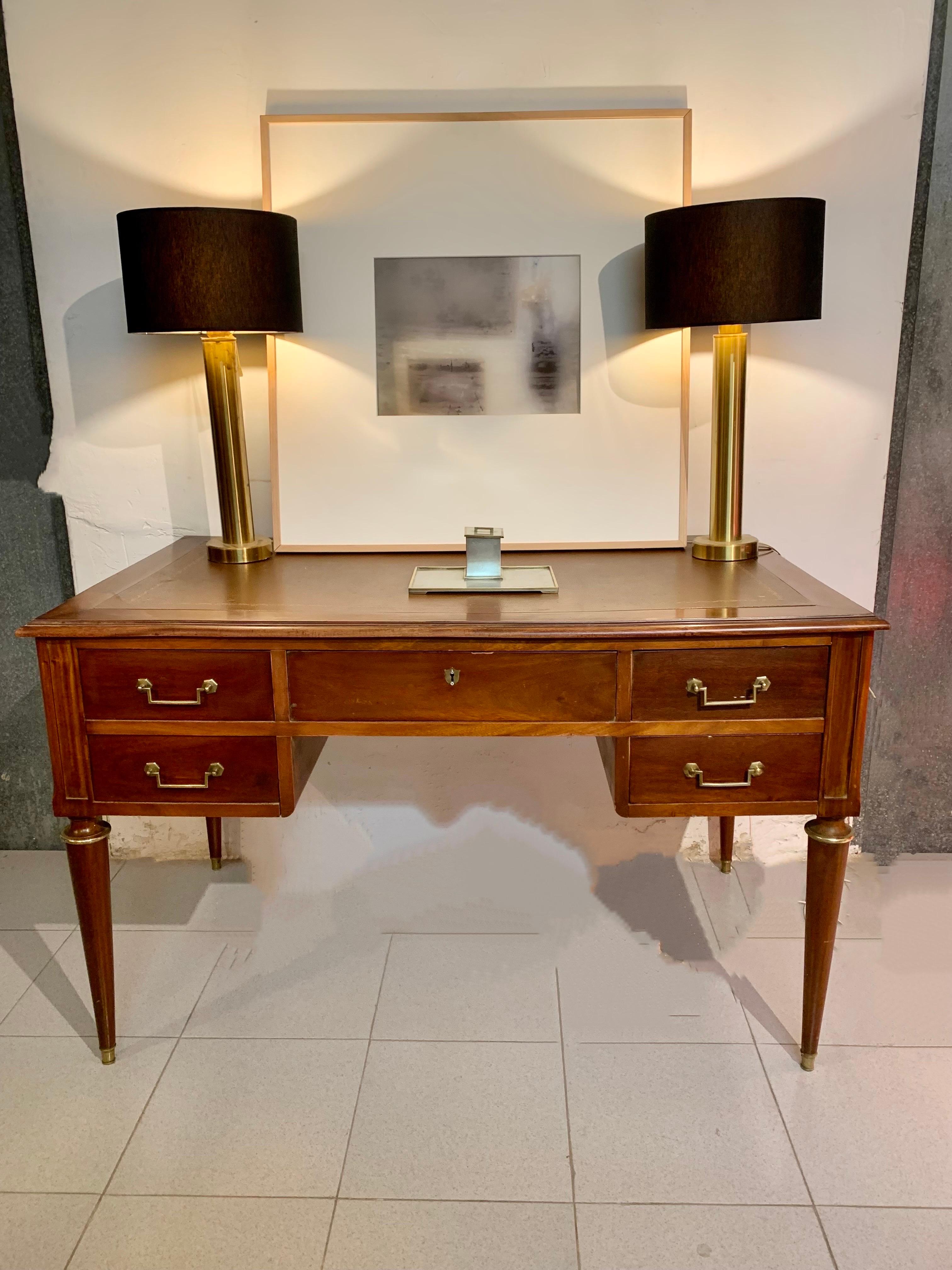 Mid-20th century Louis XVI style Spanish cherry wood writing desk features a brown leather top edged with gold filigree. It has five drawers, the main one with a brass keyhole escutcheon, the other four drawers have gilt bronze handles. Shields are