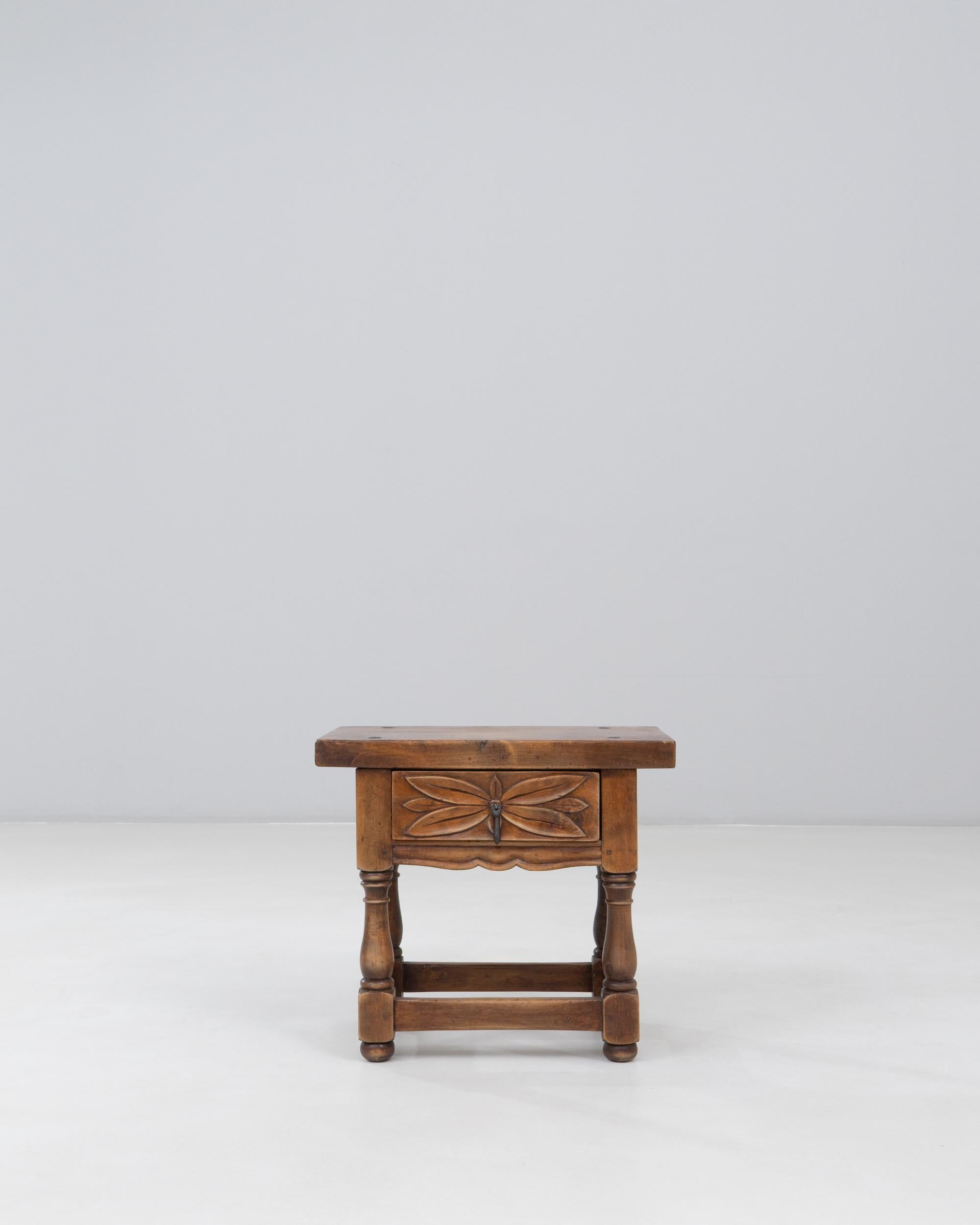 20th Century Spanish Side Table. This charming side table reflects traditional Spanish craftsmanship with its warm wood tones, robust construction, and decorative carved details. The rectangular top sits over a shaped apron adorned with a stylized