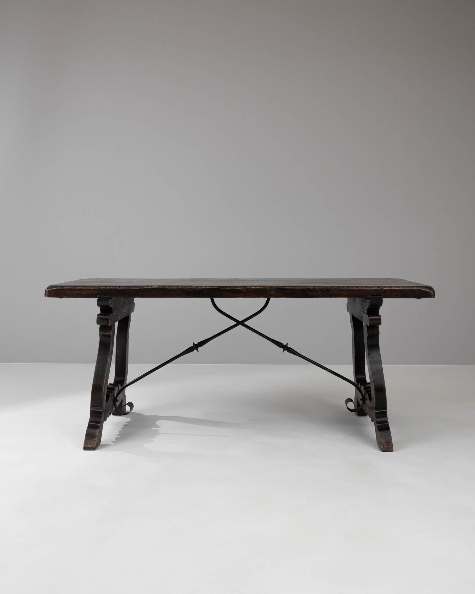This 20th-century Spanish wooden dining table carries the warmth and rustic charm of a bygone era. Crafted with sturdy, dark wood, its robust legs showcase elegant curves and ornate carvings that hark back to the detailed workmanship of traditional