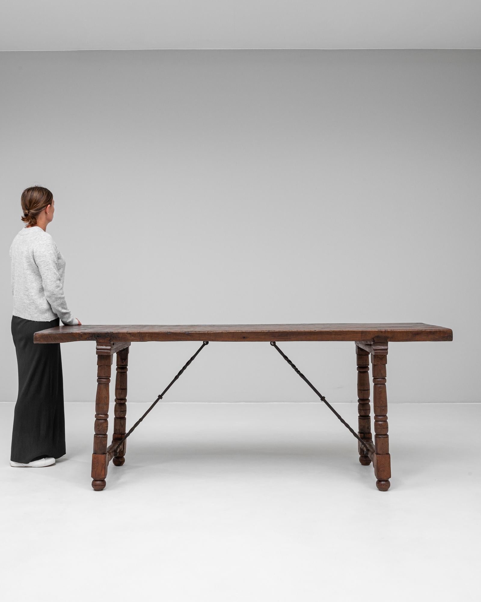 This 20th-century Spanish wooden dining table showcases rustic charm with its rich patina and solid craftsmanship. The thick, timeworn top features natural imperfections that add character, while the turned legs provide a sturdy yet elegant