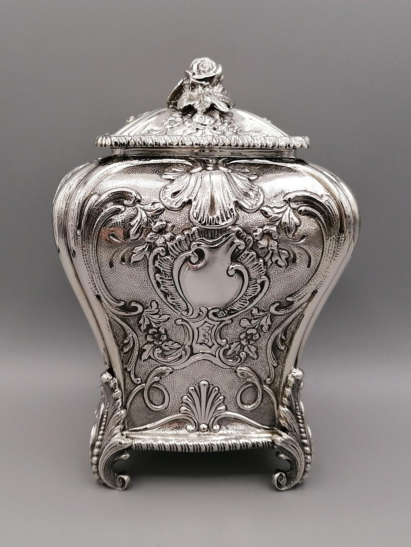 Nachbildung einer Teedose von George III. 
Sie wird aus einem Silberblech hergestellt, hat eine rechteckige Form mit geformten Seiten und ist mit floralen Motiven und Muscheln geprägt und ziseliert. Die Füße bilden Akanthusblätter nach. Der Deckel