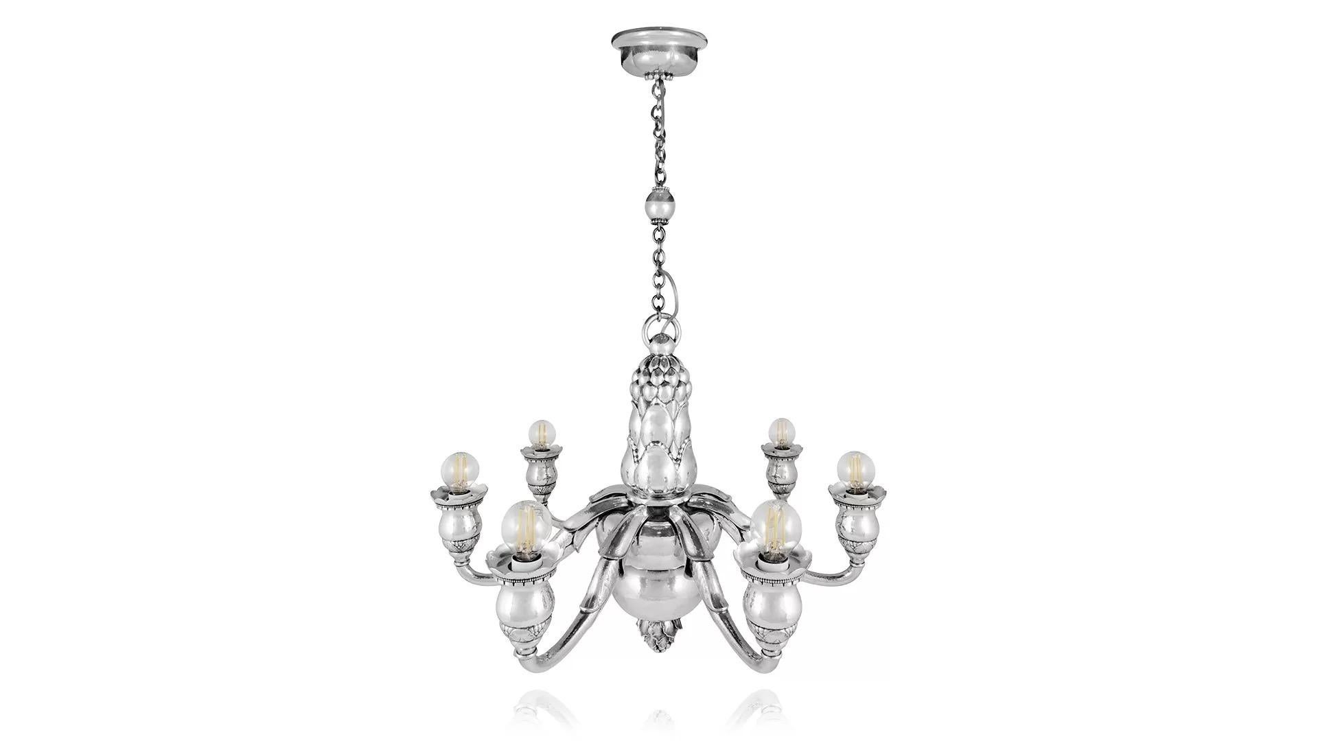 Importantísima y monumental araña de plata de ley de siete luces diseñada por Georg Jensen en 1919, que está electrificada para 220 voltios. La lámpara de araña cuelga de una cadena unida a una gran anilla a través de una bola central de plata; la