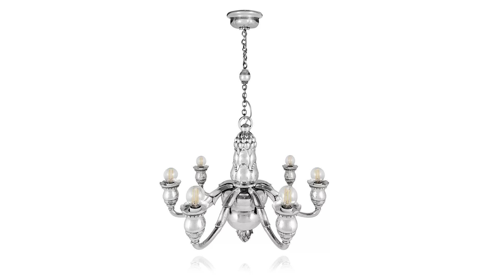 Très important et monumental lustre à sept lumières en argent sterling conçu par Georg Jensen en 1919, qui est électrifié pour 220 volts. Le lustre est suspendu à une chaîne attachée à un grand anneau par une boule centrale en argent, la colonne