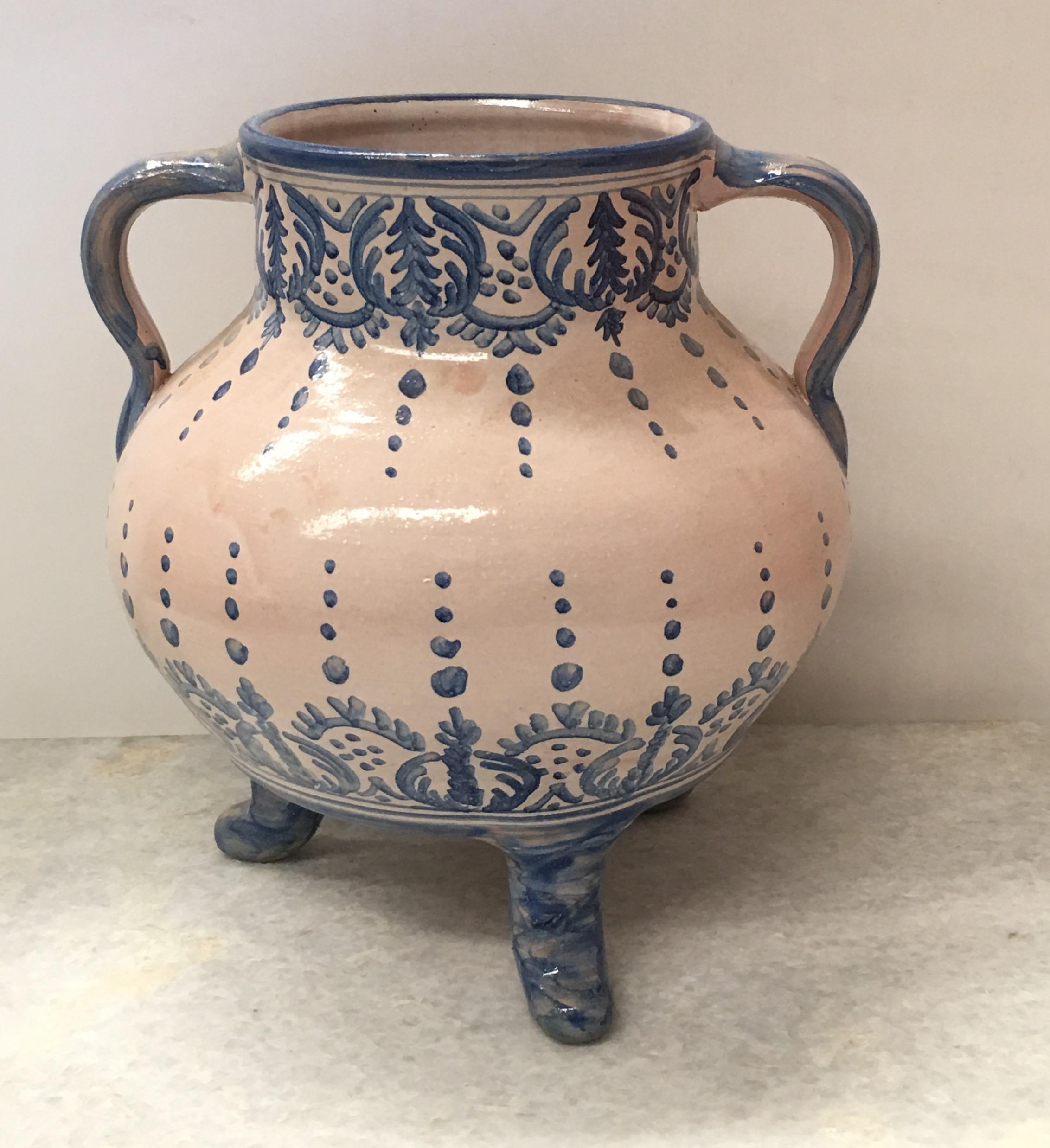 A striking Spanish glazed earthenware two-handled blue and white painted urn with foliate molded handles, the body underglaze blue decorated and three legs.