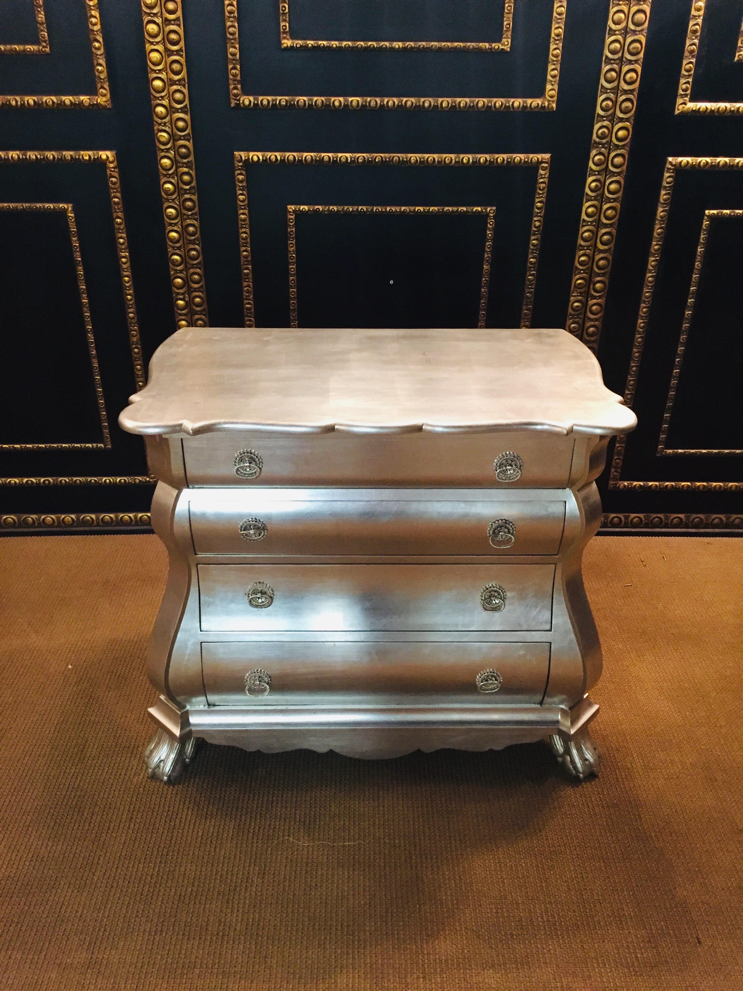 Solid wood, silver-plated on softwood. Straight body on a fitting curved frame, over sculptural carved claw feet. In the convex and concave curved front four drawers of different sizes, flanked by extended corner pilasters. Slightly protruding,