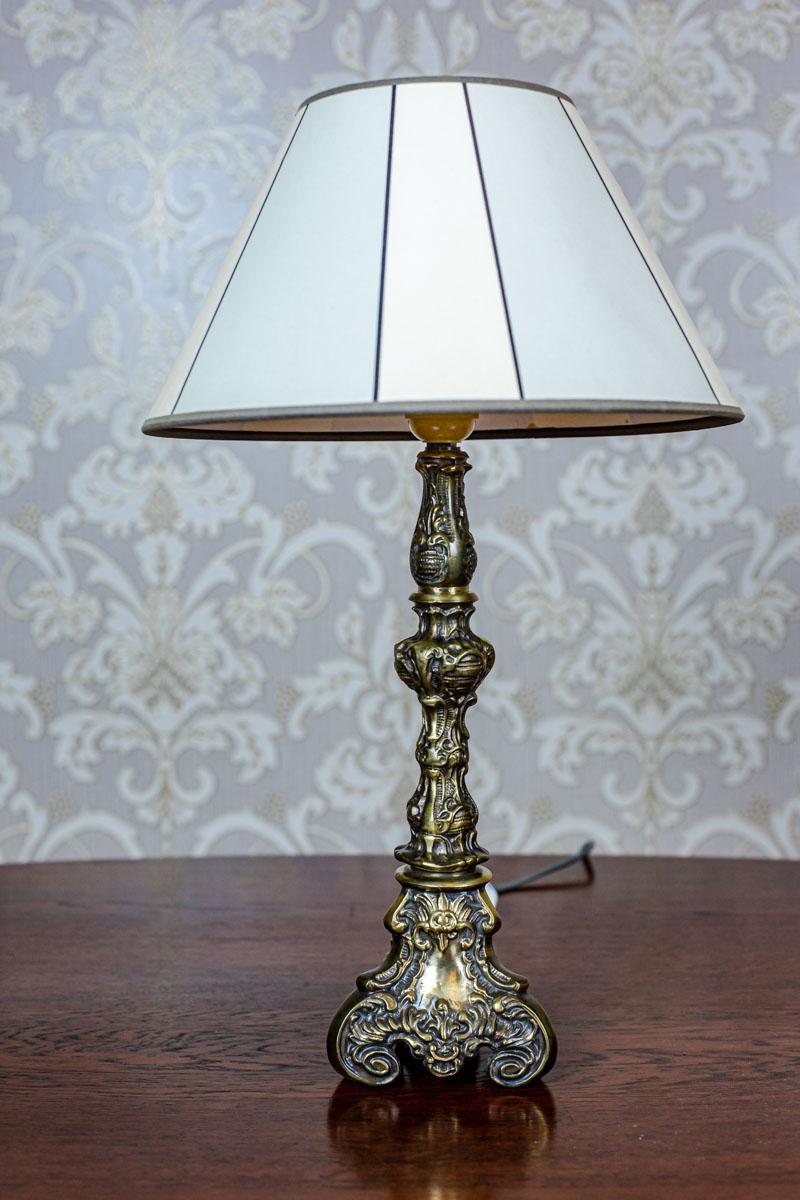 We present you a small, contemporary lamp, stylized as Neo-Rococo.
The base is made of brass, whereas the lampshade of material.

There is a socket for a single light bulb.

The power source is 230V.

This lamp is in very good condition.