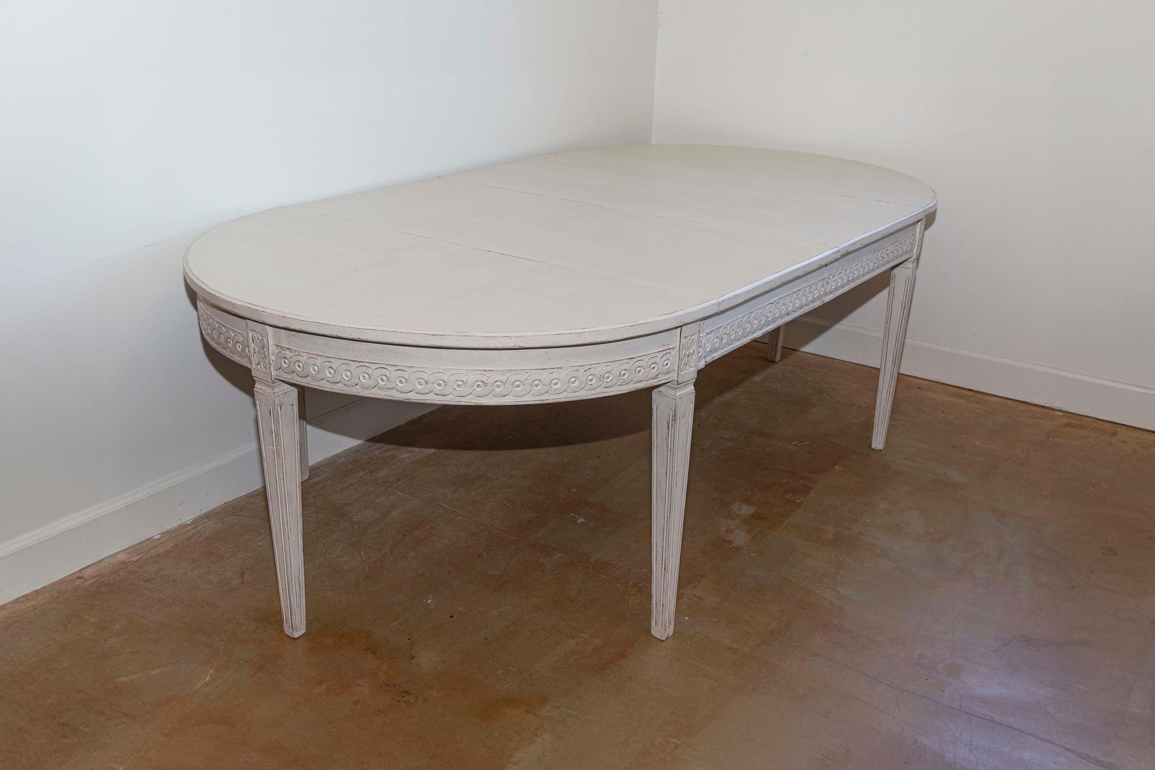Cette élégante table à rallonge suédoise du XXe siècle illustre la tradition gustavienne par son design intemporel et sa fonctionnalité. La table présente une forme ovale qui peut être rallongée par des feuilles supplémentaires, ce qui la rend