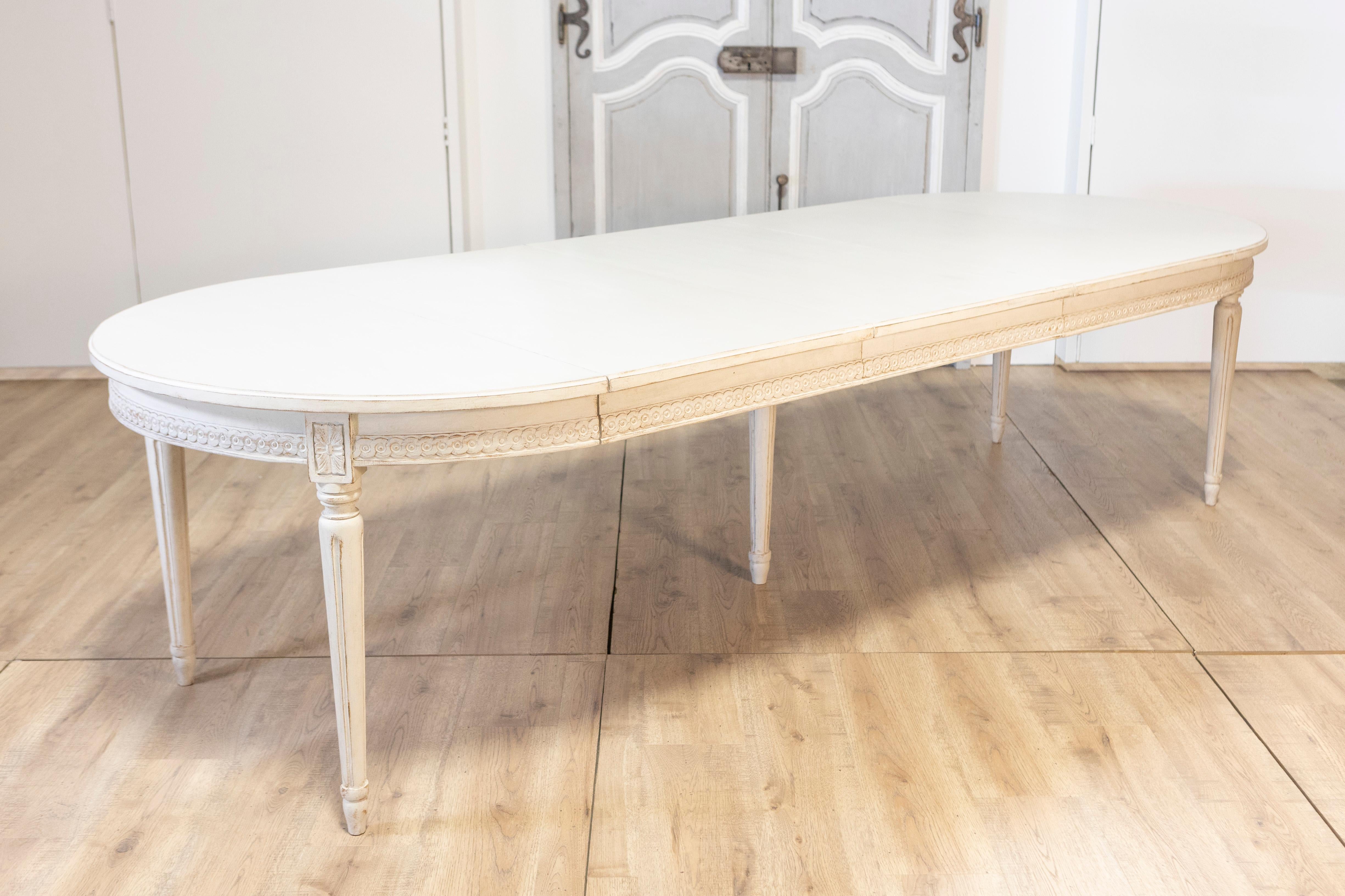 This elegant 20th-century Swedish extension dining table is a timeless example of Gustavian style, combining refined craftsmanship with practical versatility. The oval-shaped table features a delicately hand-carved apron adorned with neoclassical