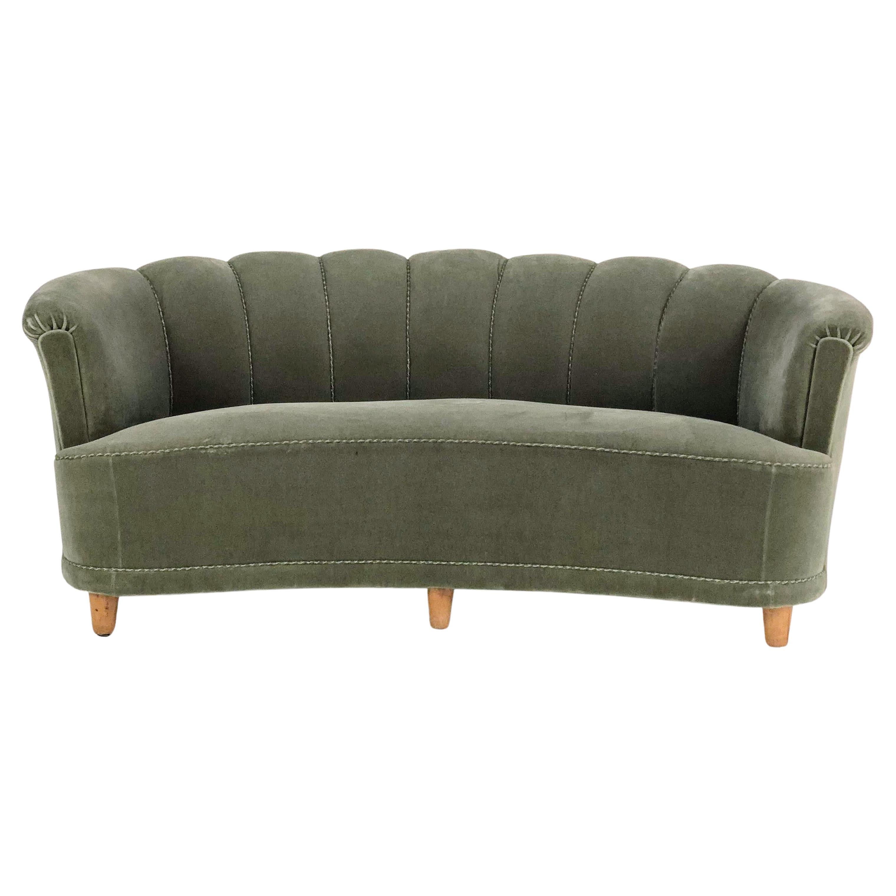 A mid-century Swedish sofa. Upholstered in an interesting green gray velour with scalloped back, piping detail on the outer edges, and 6 wooden feet. 

A pair of matching lounge chairs are also available.