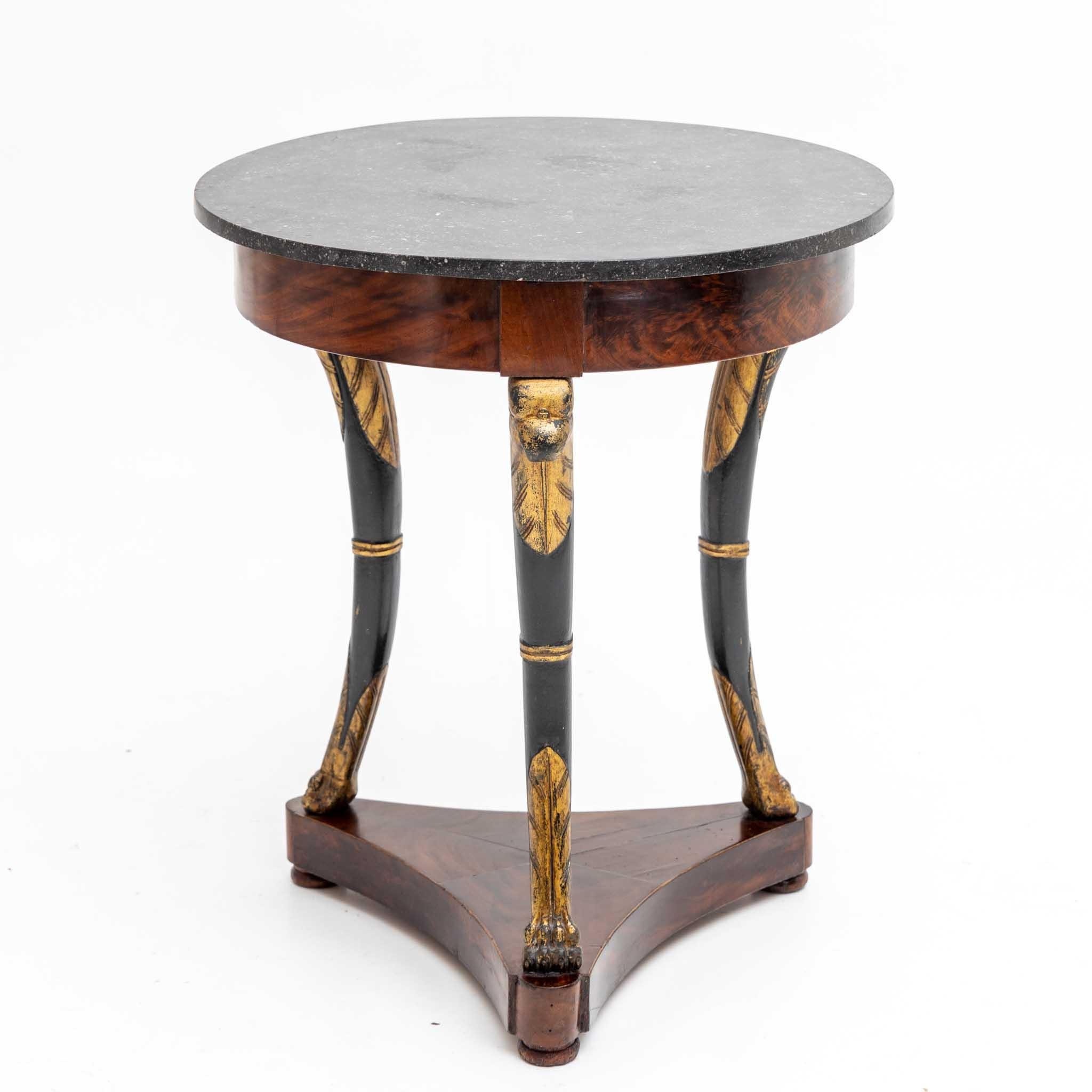 A round, antique French Empire side table made of hand crafted shellac polished, partly veneered Honduran Mahogany in good condition. The detailed small center table is composed with a black marble top, standing on three arched legs, supported by a