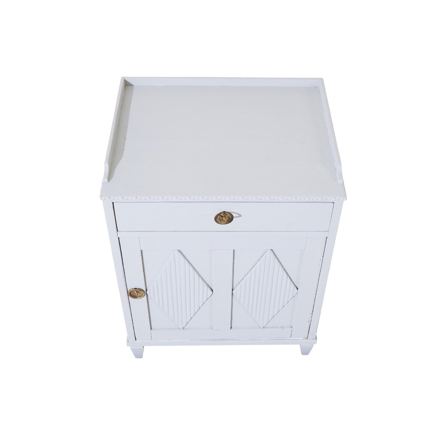 A 20th Century, single vintage Swedish Gustavian style nightstand, bed side table made of hand crafted painted Pinewood, in good condition. The detailed Scandinavian cabinet, cupboard is composed with one door and one drawer on the top, the inside