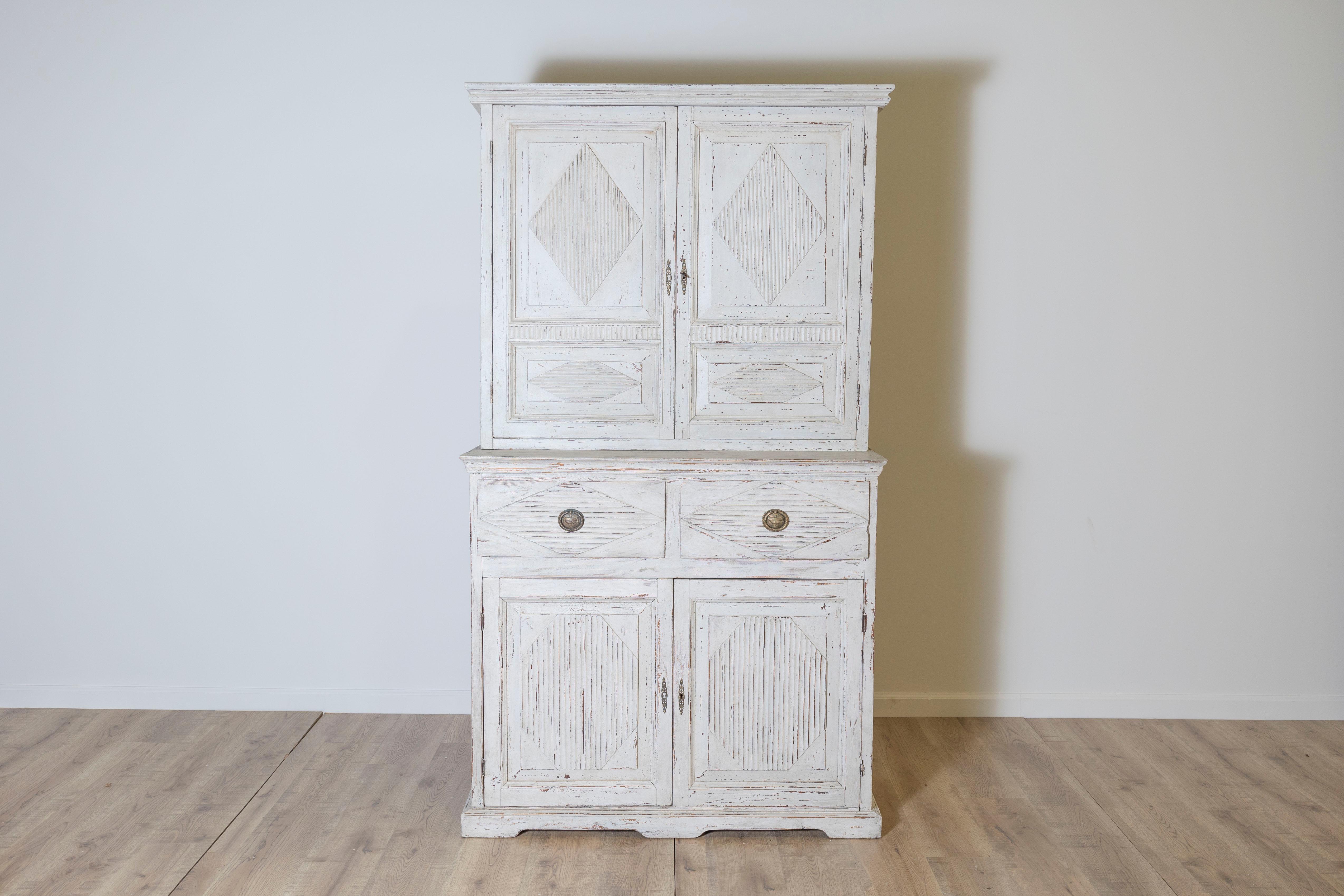 This 20th-century Swedish linen press exemplifies the charm and functionality of Gustavian-inspired furniture. Crafted from solid wood, it features clean, geometric lines with hand-carved diamond and fluted paneling, a hallmark of Swedish
