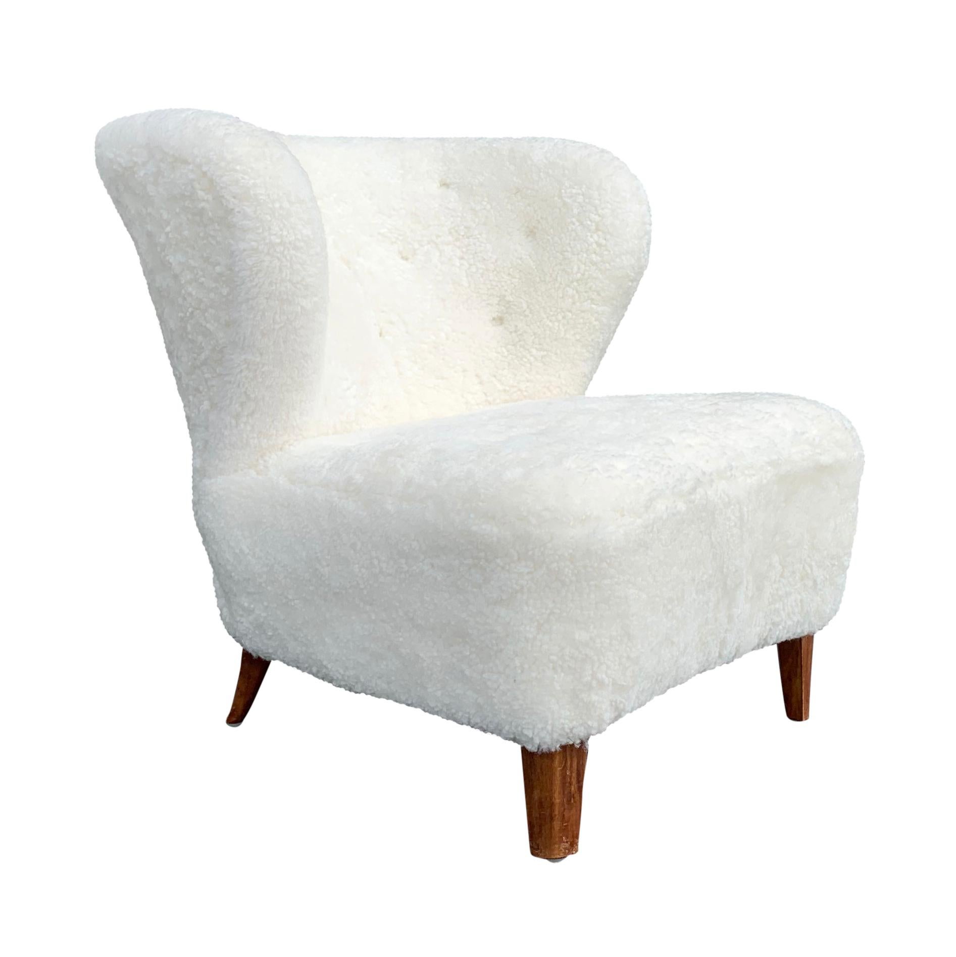 A vintage Mid-Century Modern Swedish lounge chair, designed by Goesta Jonsson and produced by Moeblering Affair, made of hand carved beechwood, in good condition. The Scandinavian side chair was newly upholstered in white sheepskin. Wear consistent