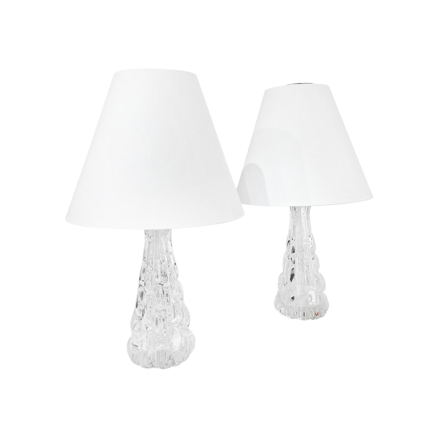 A vintage Mid-Century Modern Swedish pair of table lamps with a new white round shade, made of hand blown clear Orrefors glass, designed by Carl Fagerlund and produced, signed by Orrefors in good condition. The Scandinavian desk lights are enhanced