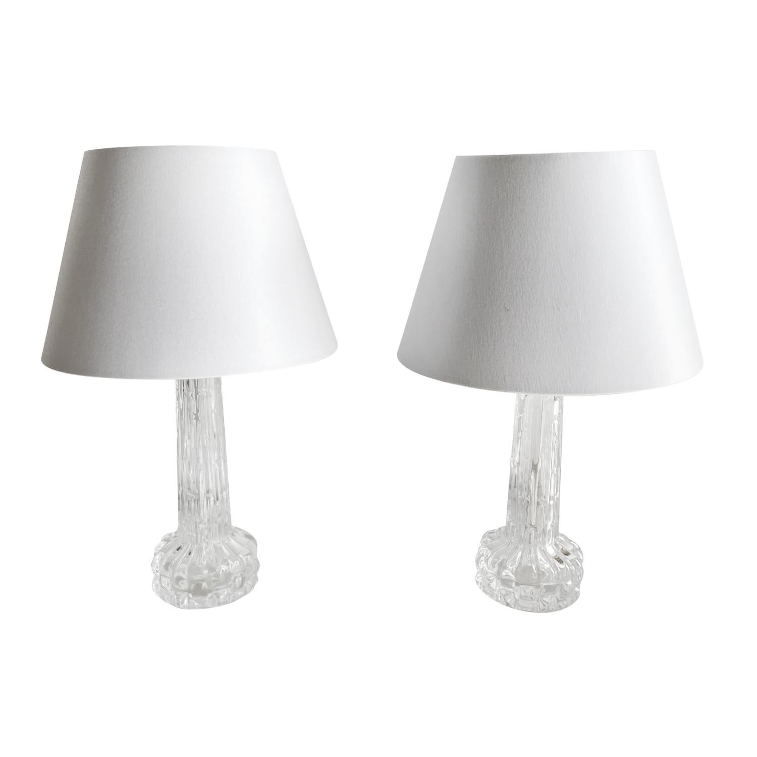 A vintage Mid-Century Modern Swedish pair of table lamps with a new round white shade, enhanced by chrome rings at the top of the stem, made hand blown clear Orrefors glass in good condition. Designed by Carl Fagerlund and produced, signed at the