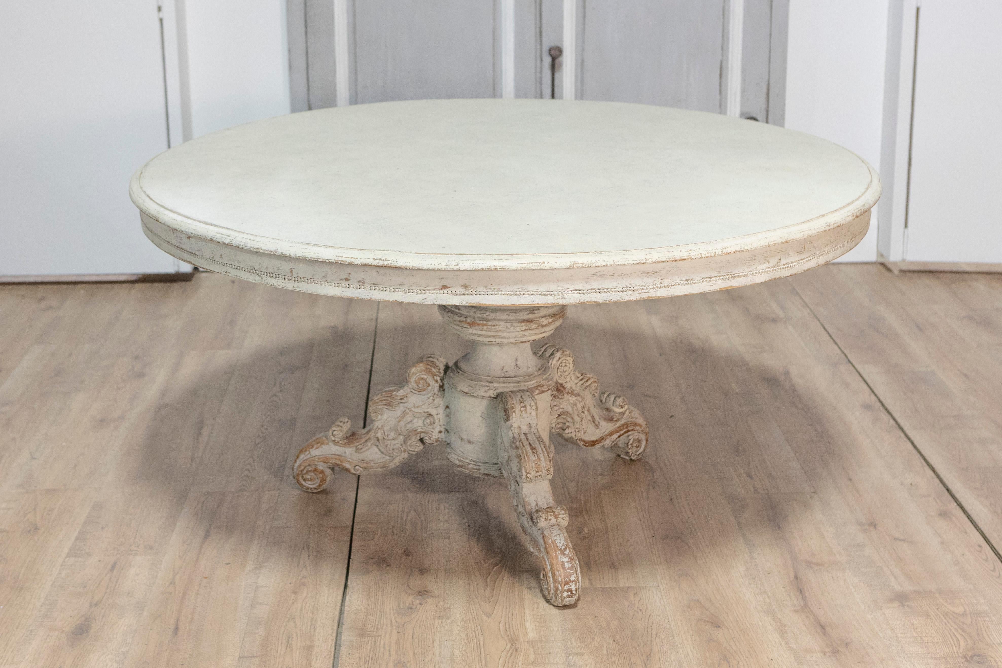 Guéridon rond suédois du XXe siècle, d'une élégance intemporelle d'inspiration gustavienne. Cette table présente une finition peinte dans un blanc doux et feutré, légèrement vieillie pour souligner son caractère vintage et apporter chaleur et charme