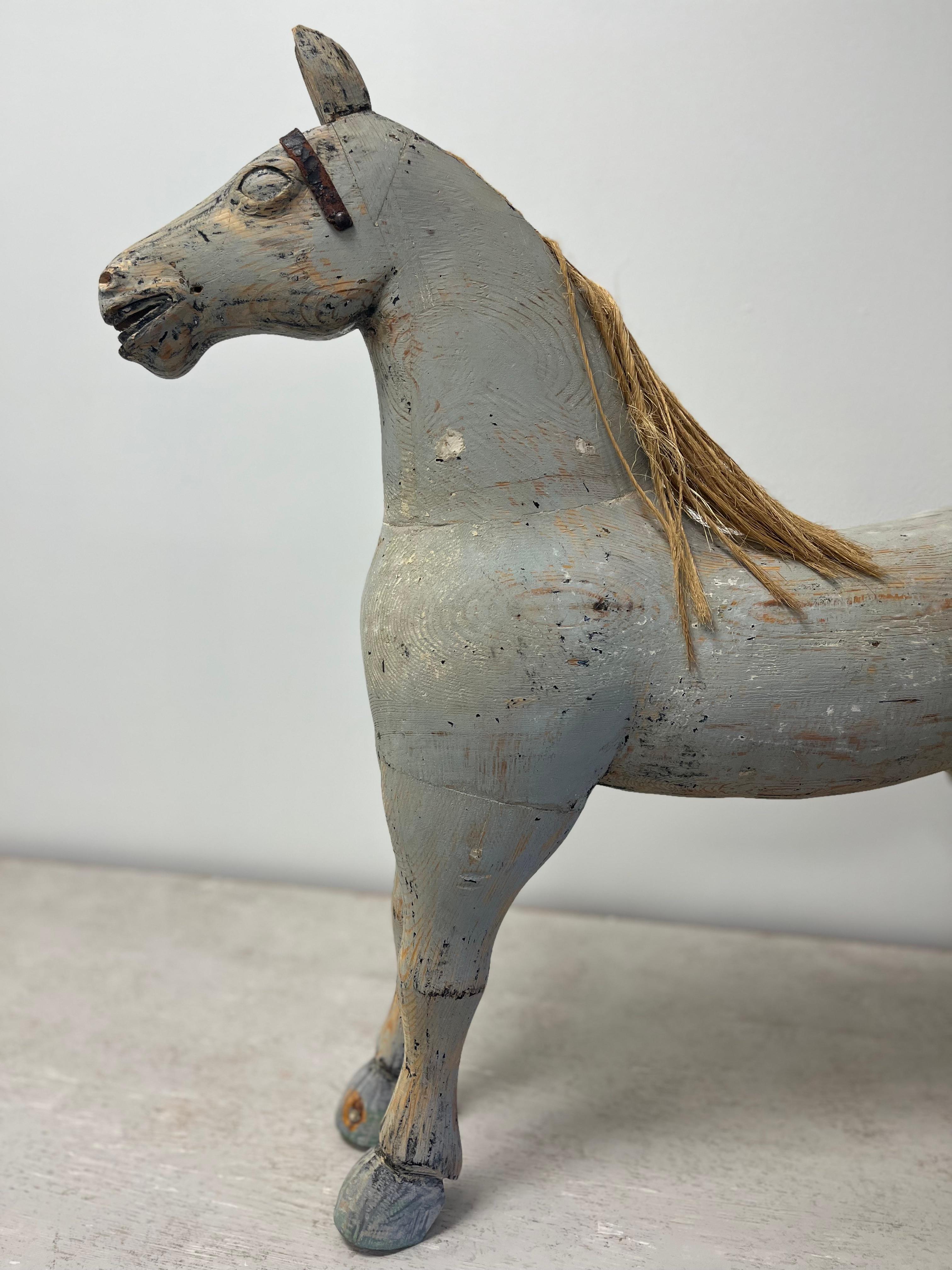 Cheval jouet suédois en bois massif, peint en gris d'origine, avec des restes de bride en cuir, de crinière et de queue en jute.